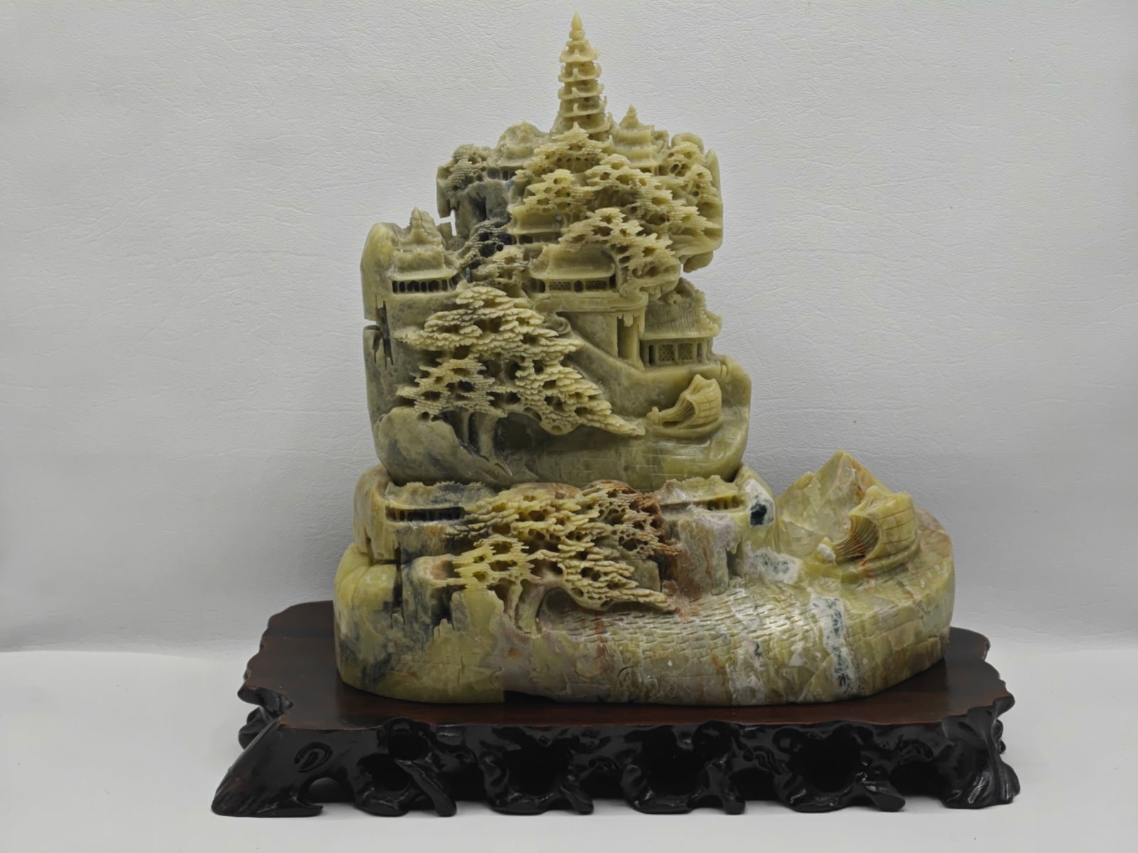Chinese Hardstone Carved Mountain Landscape Sculpture on Stand: Chinese carved hardstone sculpture depicting a mountainous landscape with pagodas, trees, and figures, intricately worked in relief with naturalistic coloration of the stone, mounted on a carved woode