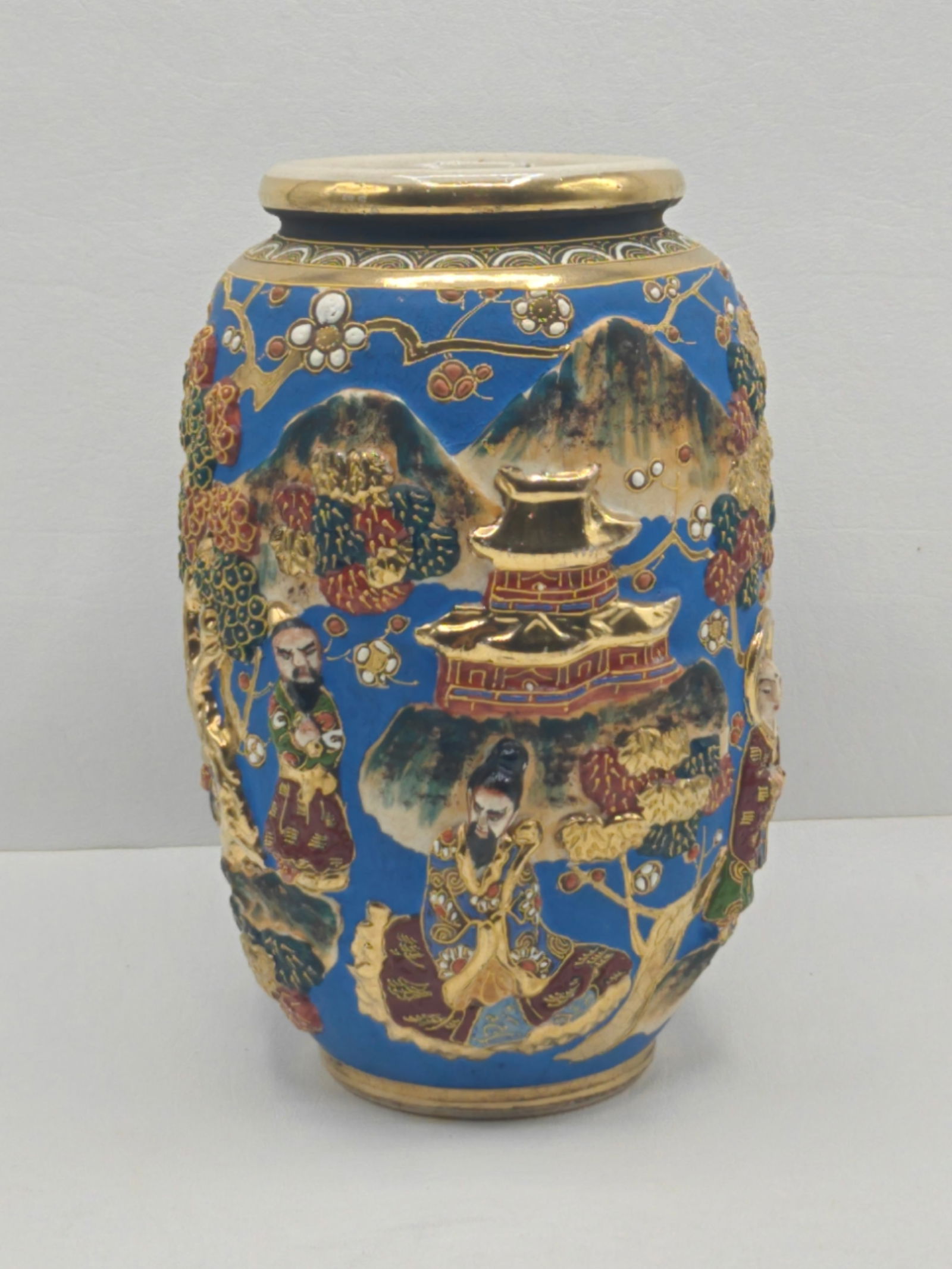 Japanese Satsuma Earthenware Vase with Figural Decoration: Japanese Satsuma earthenware vase decorated with raised enamel and gilt depicting figures in a mountainous landscape with trees and architecture on a rich blue ground, detailed with gilt highlights an
