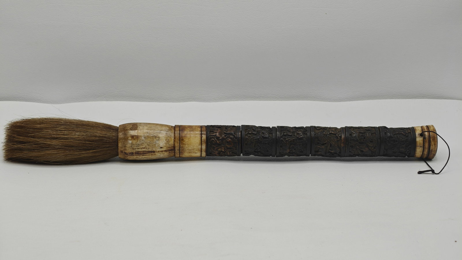 Chinese Carved Bone Handle Calligraphy Brush with Figural Relief: Traditional Chinese calligraphy brush featuring a finely carved bone handle with detailed figural and mythological relief decoration in segmented panels. The handle shows rich dark patina contrasting
