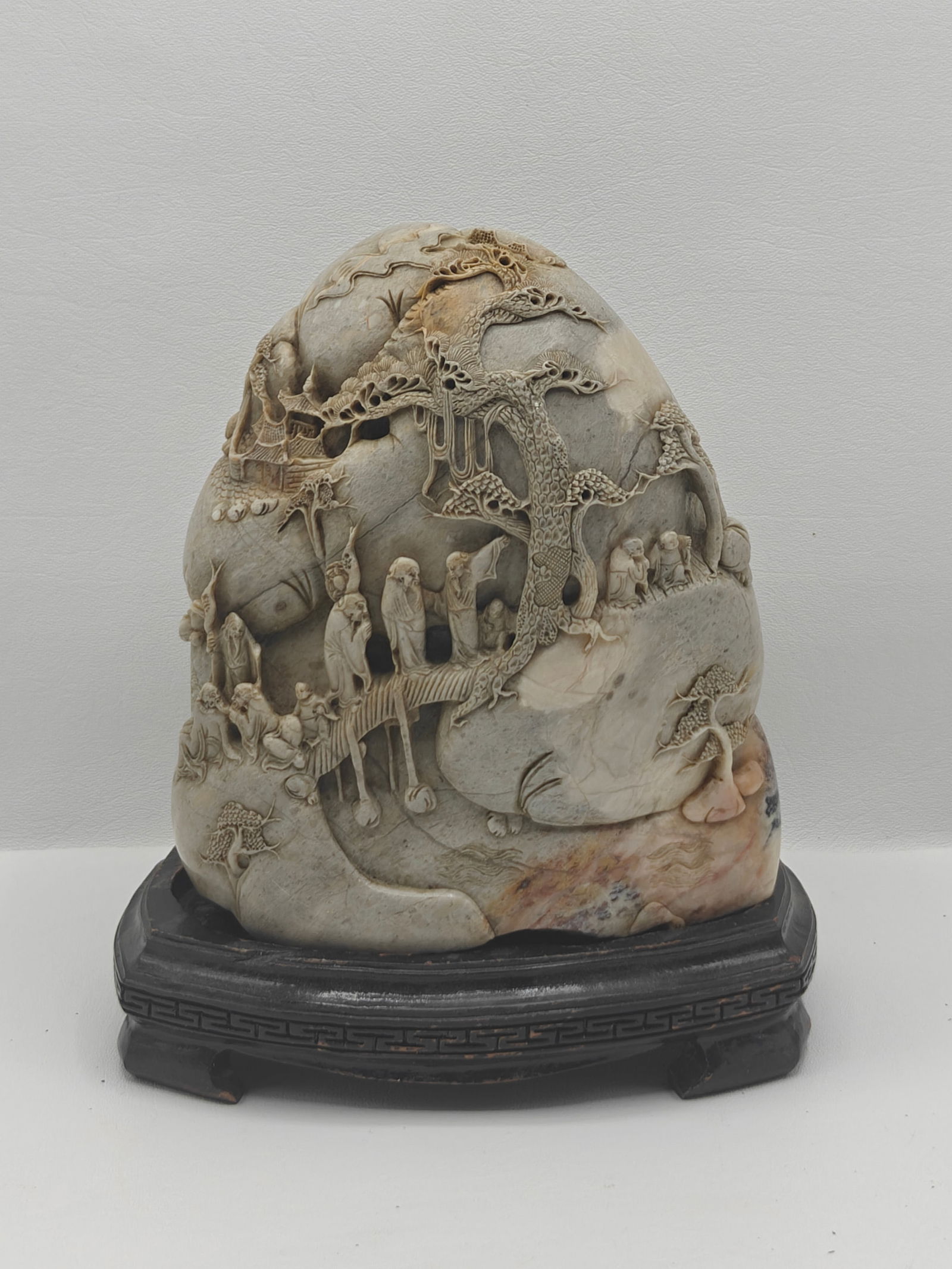Chinese Carved Hardstone Landscape Sculpture on Wood Stand: Finely carved Chinese hardstone sculpture depicting a detailed mountainous landscape scene with scholars, attendants, pavilions, and trees in high relief. The carving features layered rock formations