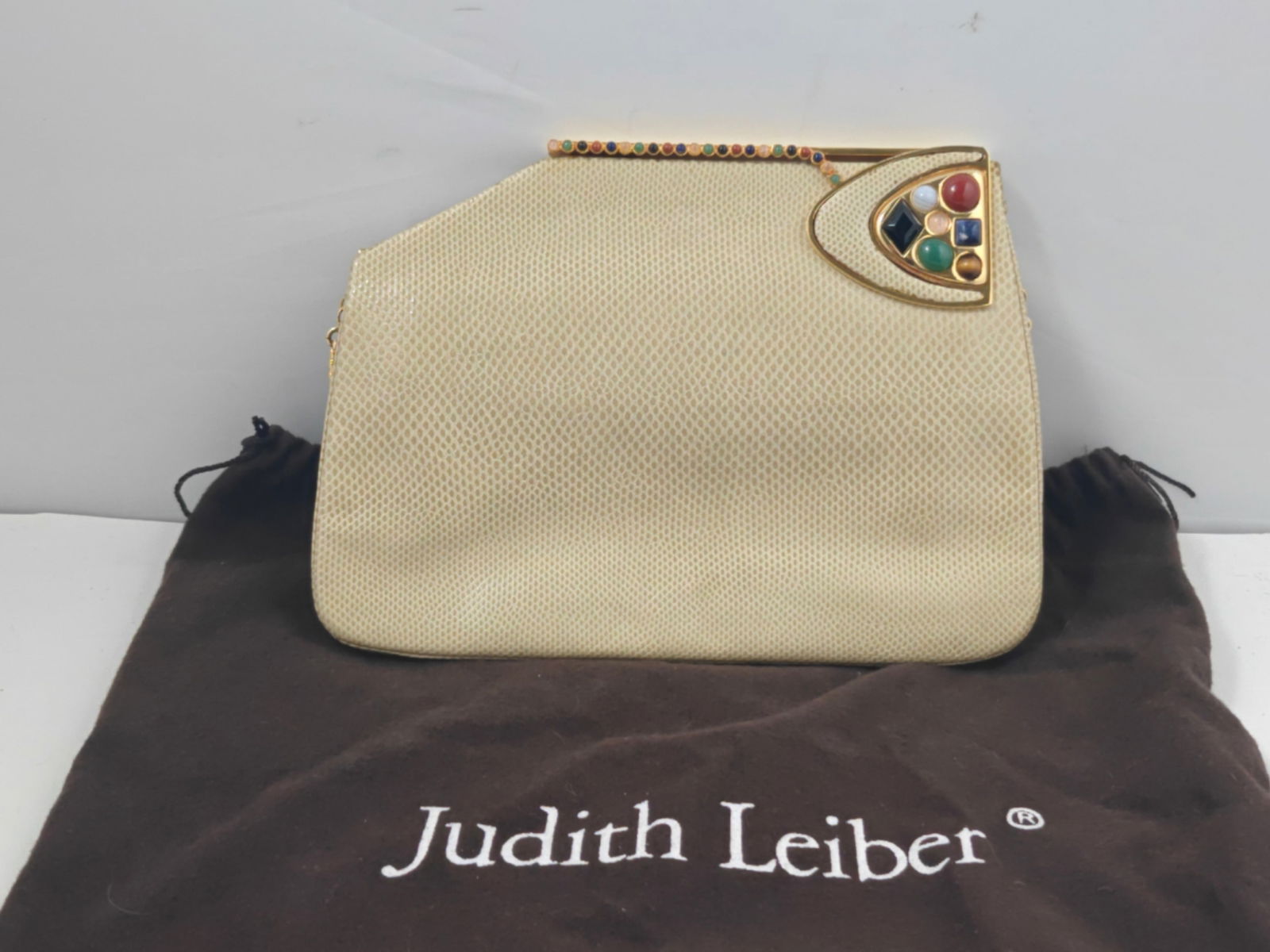 Vintage Judith Leiber Snakeskin Evening Clutch with Multi-Stone Clasp, Chain Strap, Box & Dust Bag: Vintage Judith Leiber evening clutch in cream-toned snakeskin with a structured geometric silhouette. Features a gold-tone frame with an asymmetrical corner clasp set with multicolored cabochon and fa
