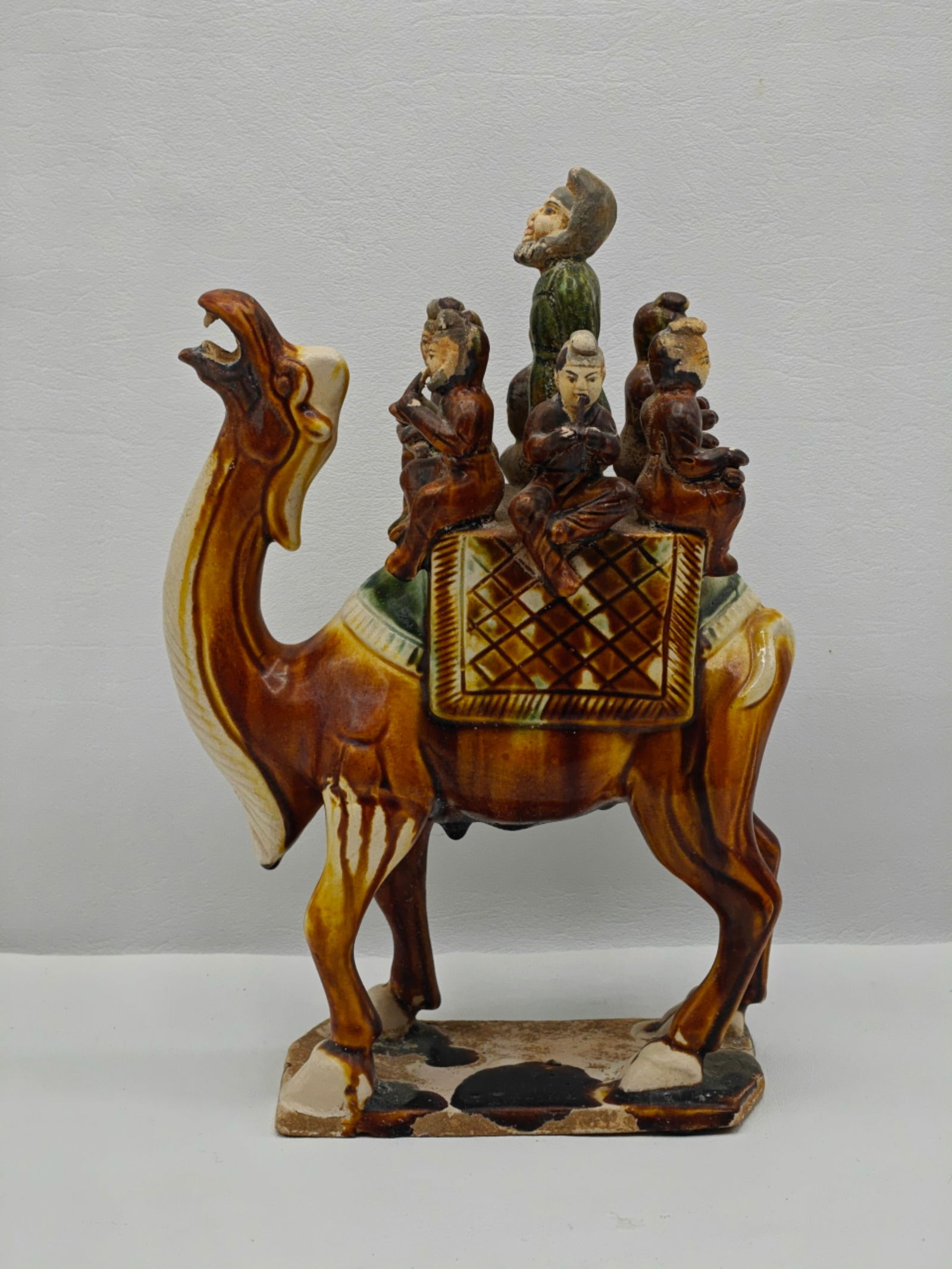Chinese Tang Style Sancai Glazed Camel with Riders: Modeled after Tang dynasty trade caravan figures, this ceramic camel carries multiple riders and attendants, decorated in traditional sancai (three-color) glaze with amber, green, and cream tones, app
