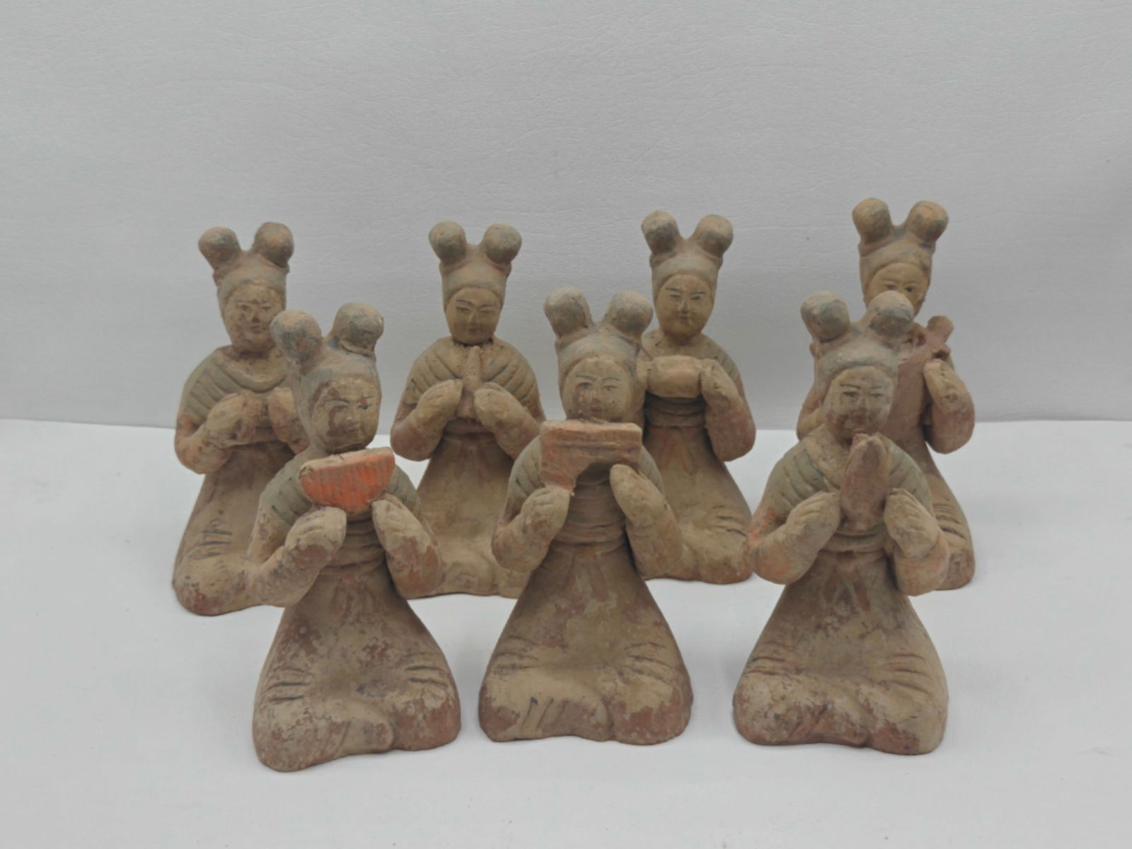 Set of Seven Chinese Tang Dynasty Style Pottery Lady Musicians: Group of seven seated female musician figures in Tang dynasty taste, each modeled holding instruments or ceremonial objects, with characteristic high coiffures and flowing robes, retaining traces of o