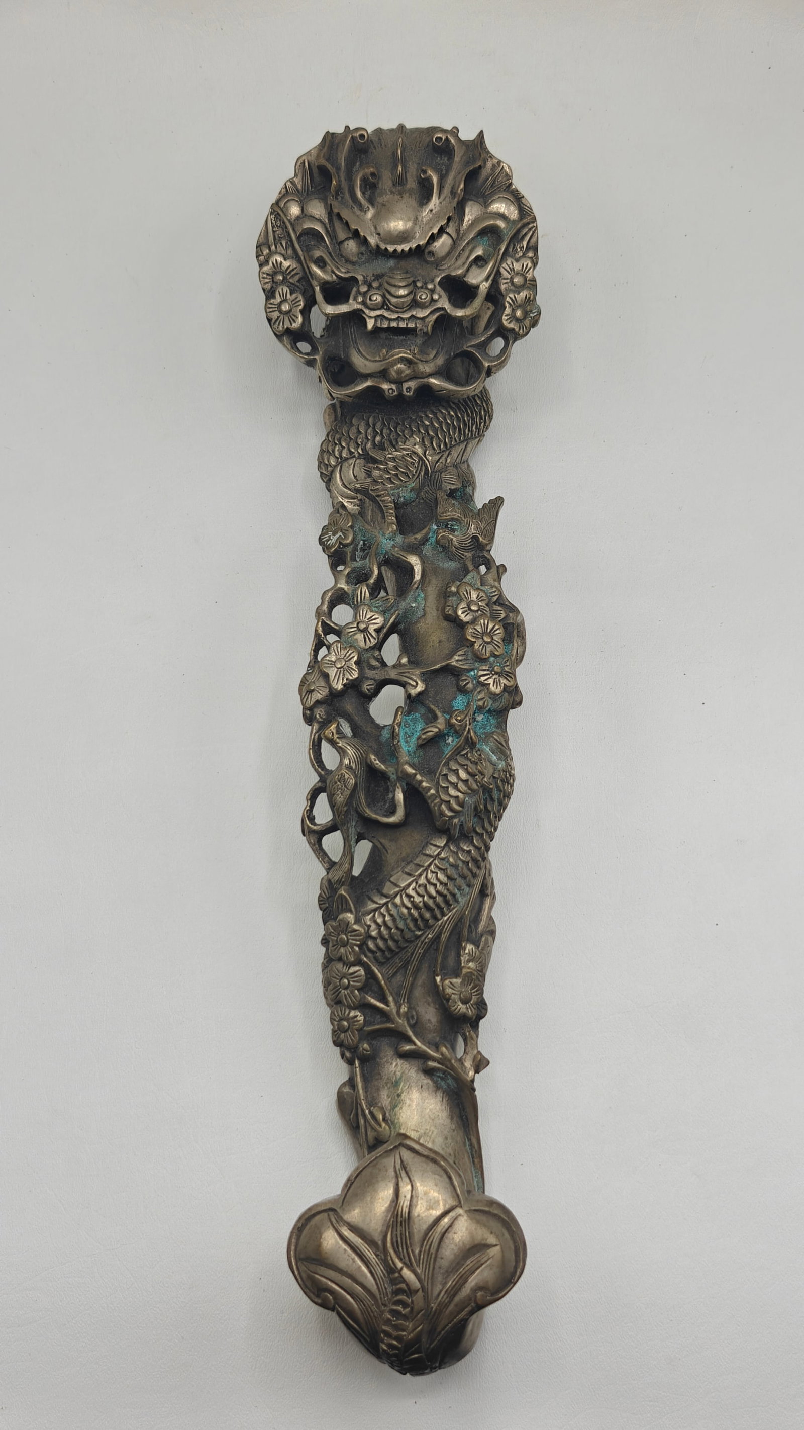 Chinese Gilt Bronze Ruyi Scepter with Dragon and Floral Motifs: Elongated ruyi-form scepter cast in relief with a sinuous dragon amidst flowering branches and birds, the handle terminating in a stylized lingzhi-head form, with openwork details and traces of gilt s