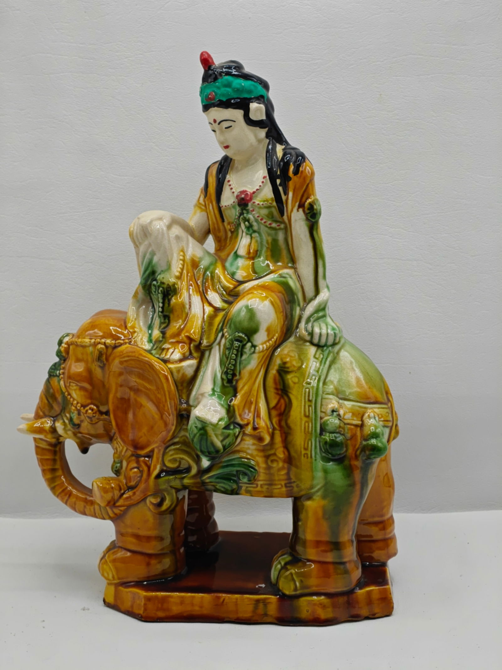 Chinese Sancai-Glazed Pottery Figure of Puxian (Samantabhadra): Modeled as the bodhisattva Puxian seated in relaxed pose atop a caparisoned elephant, covered in sancai-style glazes of amber, green, and cream tones, raised on an integral base. 20th century decorati