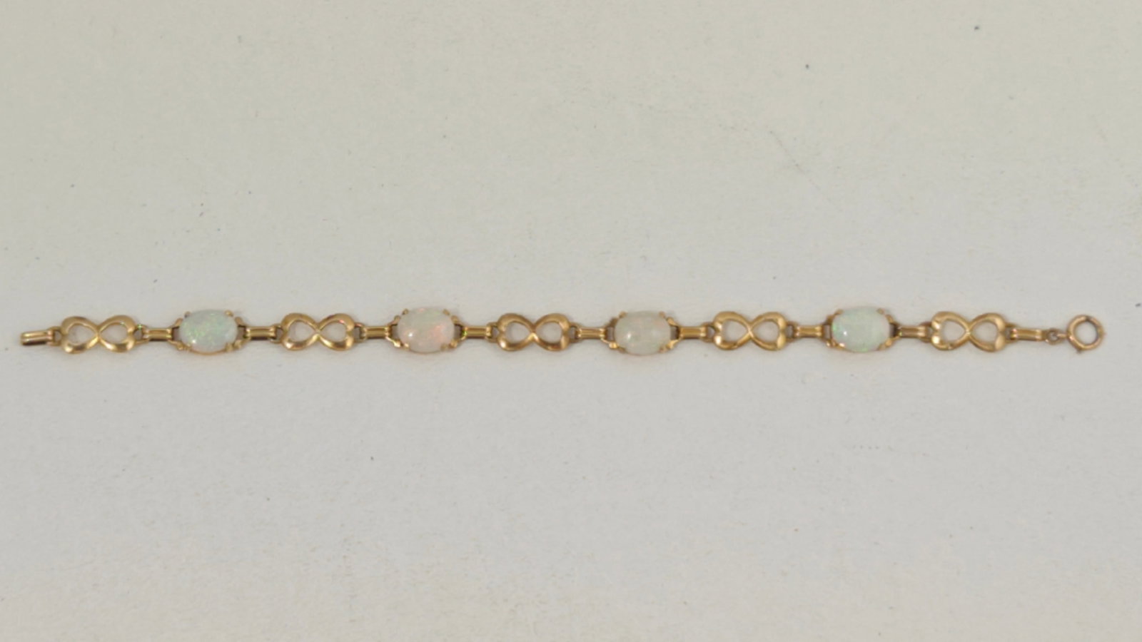 14K Gold Opal Link Bracelet: 14K yellow gold link bracelet featuring four oval cabochon opals displaying subtle play-of-color, interspersed with infinity-style links. Measures approximately 7.5 inches in length and weighs 8.74 gr