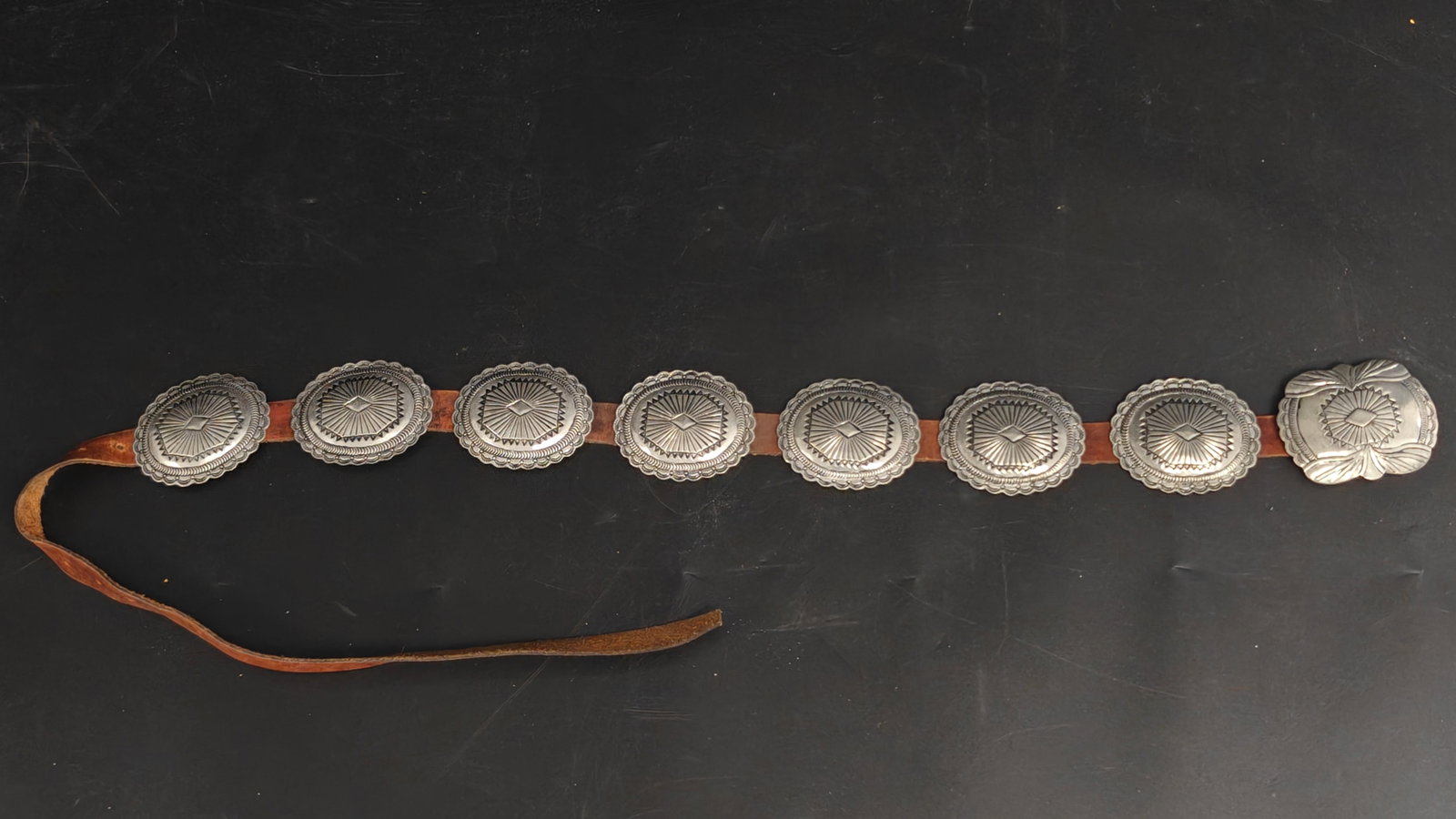 Vintage Southwestern Style Concho Belt: Vintage Southwestern-style concho belt featuring eight hand-tooled oval conchos and a larger matching buckle mounted on a rich brown leather strap. Each silver-toned concho is decorated with tradition