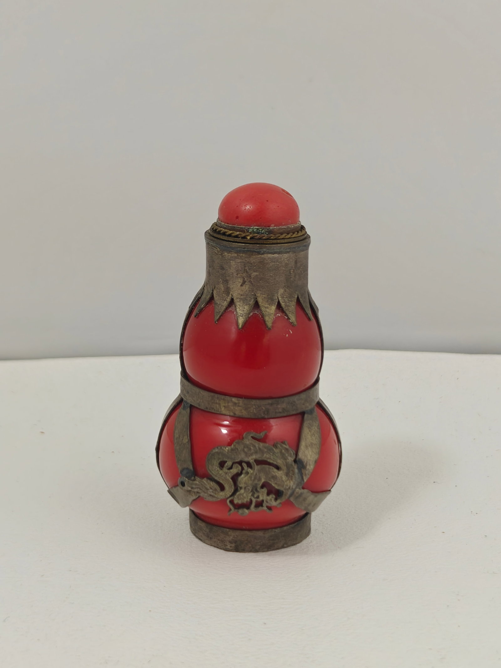 Chinese Red Resin Double Gourd Snuff Bottle with Dragon Mounts: Vintage Chinese gourd-form snuff bottle crafted from translucent red resin and mounted with silver-toned metal fittings featuring an applied dragon motif. Retains its matching stopper with attached sp