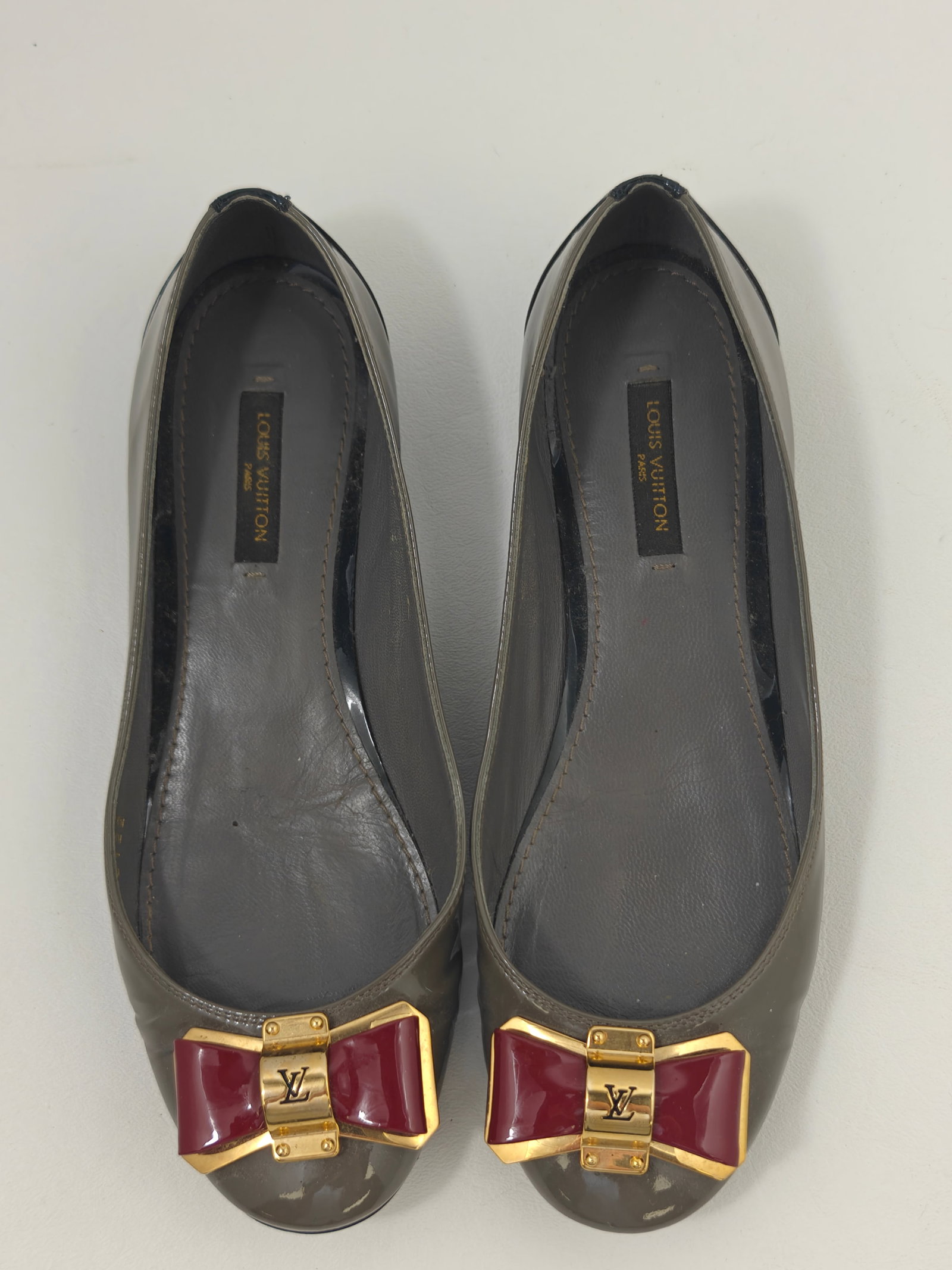 Authentic Louis Vuitton Grey Patent Leather Bow Ballet Flats, Size 36: Authentic Louis Vuitton ballet flats crafted in grey patent leather with contrasting black patent leather heel panels and signature burgundy patent leather bow accents set in gold-tone Louis Vuitton l
