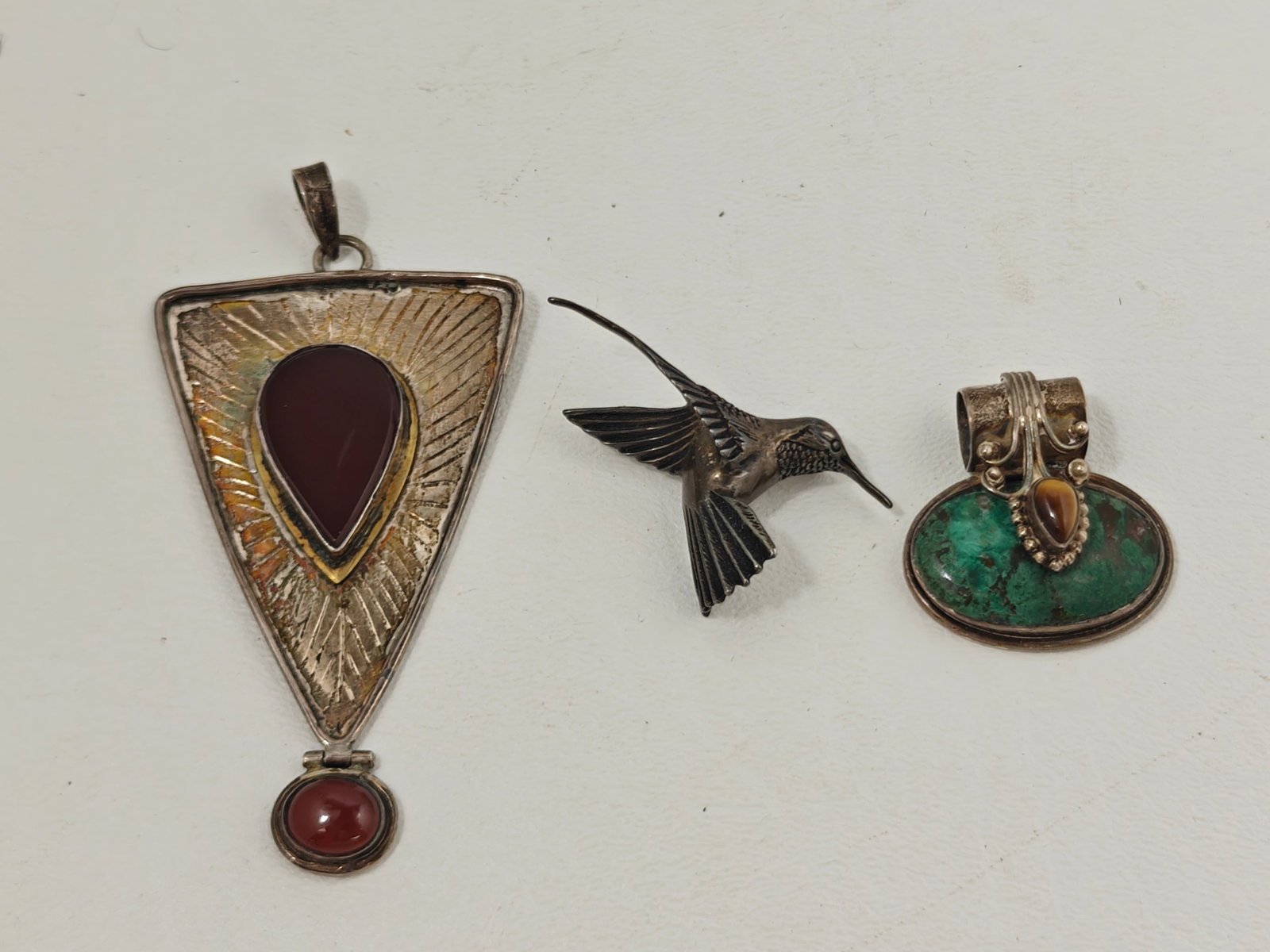 Sterling Silver Jewelry Group with Carnelian, Chrysocolla & Hummingbird Brooch: Group of three sterling silver jewelry pieces including a large modernist pendant set with two cabochon carnelians, a Southwestern-style pendant set with an oval chrysocolla stone and tiger's eye cabo