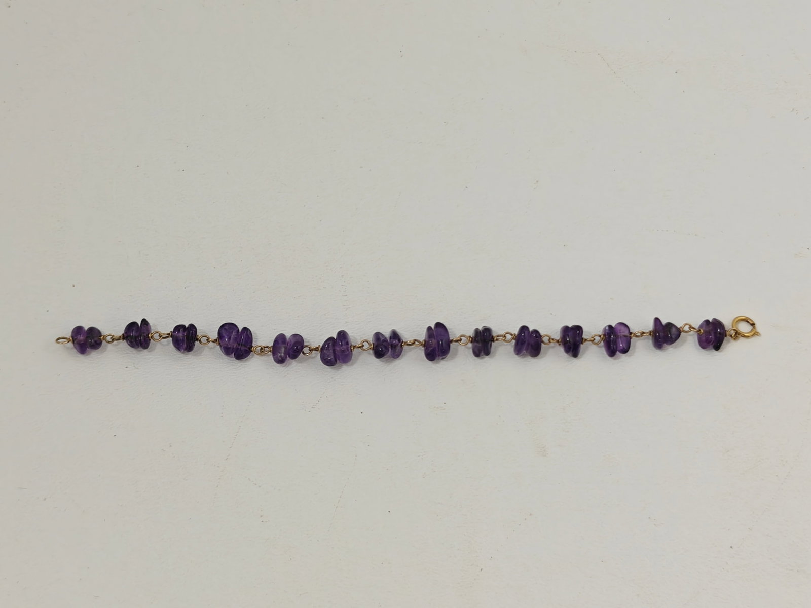 Amethyst Chip Bead Bracelet, 14K Gold Clasp: Seven-inch bracelet comprised of polished natural amethyst chip beads linked with 14K yellow gold wire connectors and fitted with a spring ring clasp stamped "14K." The amethyst displays medium to dee
