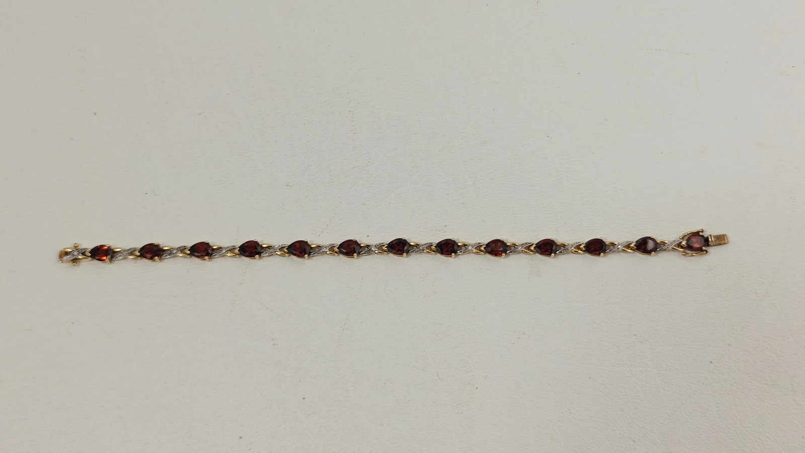 10K Gold Garnet and Diamond Link Bracelet, 7.25 In.: Stamped 10K, this yellow gold bracelet features a series of pear-shaped garnets in prong settings, joined by graceful X-form links accented with small round diamonds. The alternating garnet and diamon