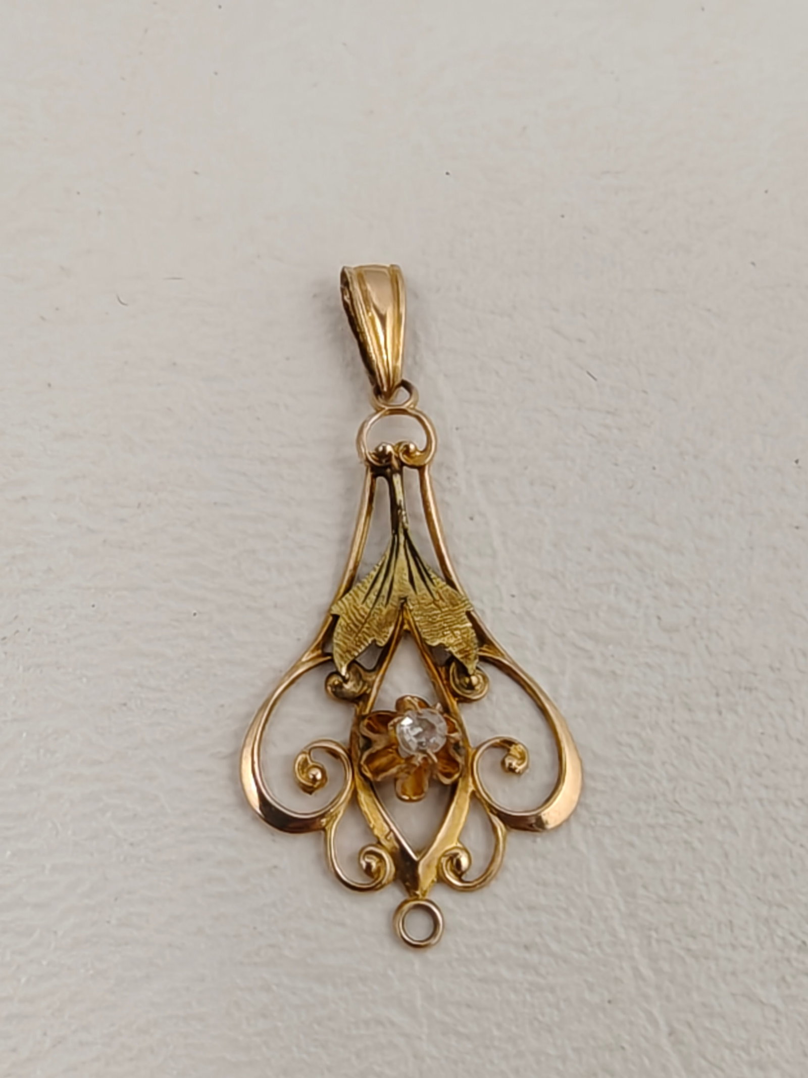 Vintage 10K Yellow Gold Filigree Diamond Pendant: Delicate vintage pendant crafted in 10K yellow gold with an elegant openwork filigree design accented by engraved leaf motifs. The center features a small round diamond set within a flower-form mounti