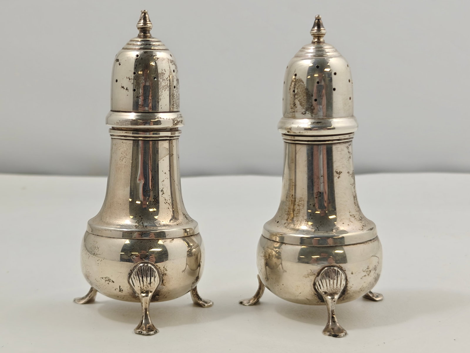 Sterling Silver B. & M. Footed Salt & Pepper Shakers, Pair: Pair of matching sterling silver salt and pepper shakers by B. & M., each raised on three shell-form feet with baluster bodies and domed pierced tops with urn-form finials. Marked "B. & M. Sterling 43