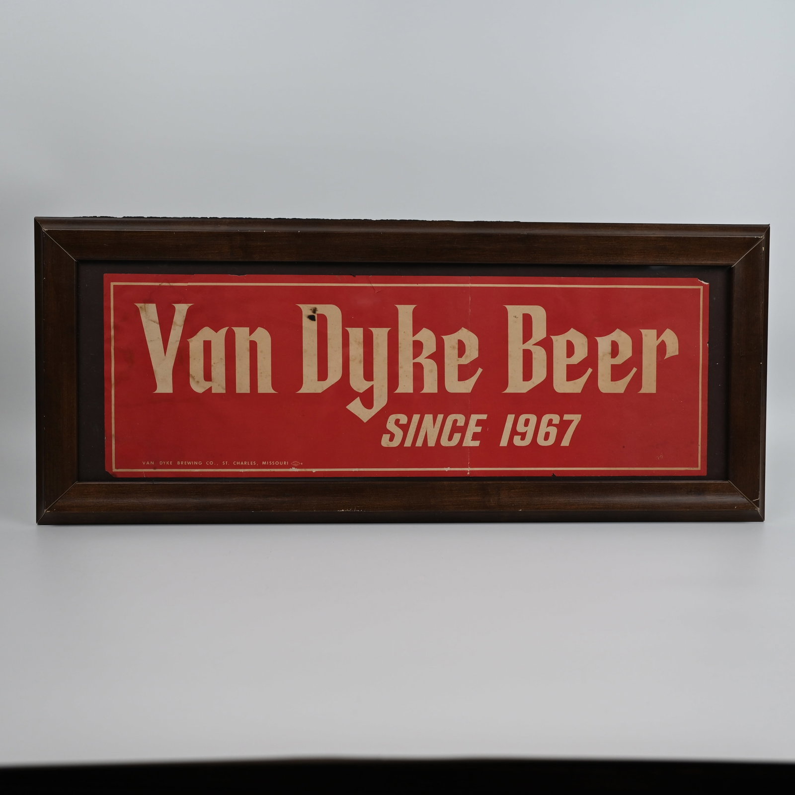 Van Dyke Beer - St Charles Missouri Paper Advertising Sign: The Van Dyke Brewing Company was in operation 1967 - 1970. Per online resources, the company never reported a profit and quickly closed. Visible area of image: 7 H inches x 20 7/8 W inches. Framed to 