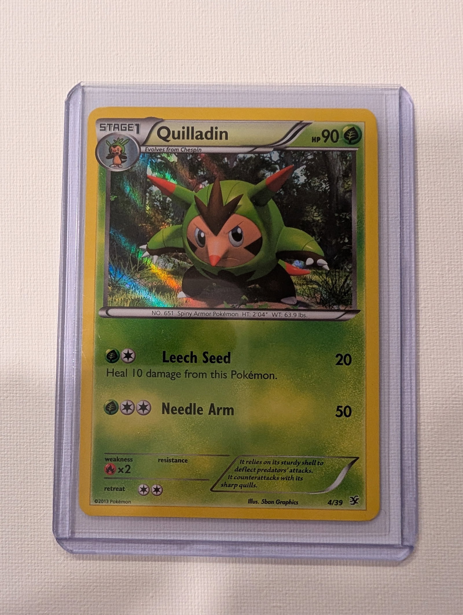 2013 Pokemon Quilladin 4 39 XY Kalos Starter Set Holo.: This lot is a Quilladin Holo card numbered 4 39 from the 2013 XY Kalos Starter Set. It is a Grass type Stage 1 Pokemon with 90 HP that evolves from Chespin and features artwork by 5ban Graphics. The