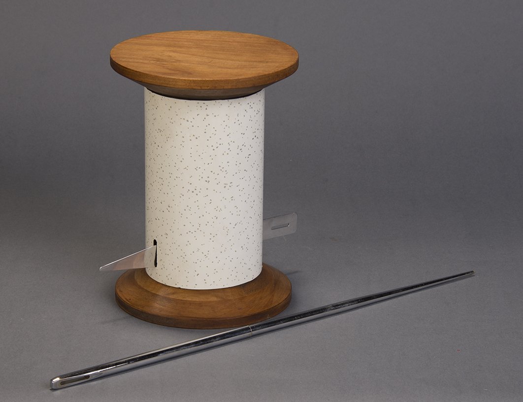 Through The Needle - Owen Magic Supreme: A giant, stainless steel sewing needle is examined by the audience. A ribbon is threaded through slots is a large wooden spool. The needle is lowered into the hole at the top of the spool, never fully