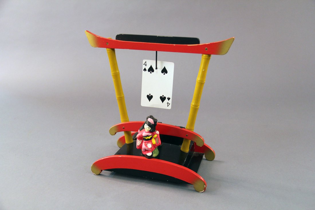 Fan-Ta-Card - Mazda Magic: 1952. A card is selected and returned to the deck. A decorative Asian-styled framework is shown and held by the magician. Suddenly there is a bang! The selected card reappears hanging on a hook at the