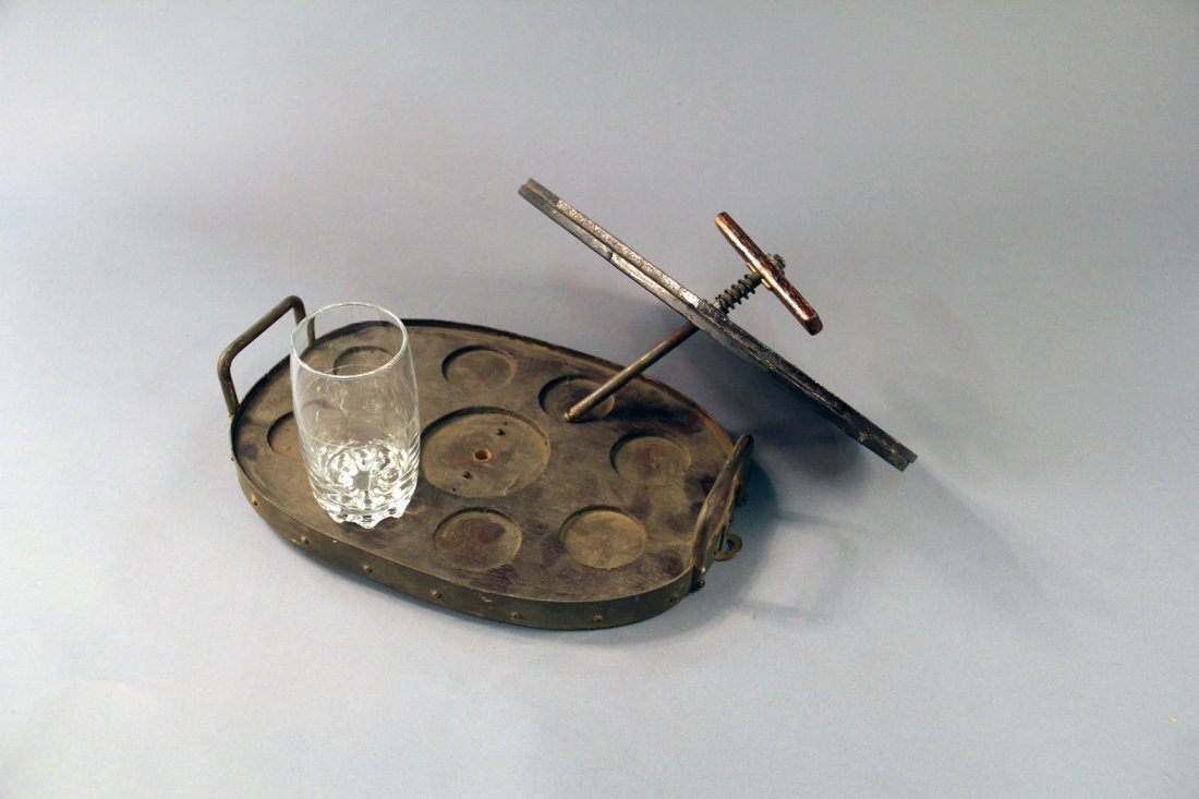 Tray of Glasses Production: Circa 1910. Heavily built, wooden and steel tray that holds 8 unprepared glasses (not included) filled with liquid. Glasses are pre-set on the tray and then clamped in-place with a rubber-lined lid wi