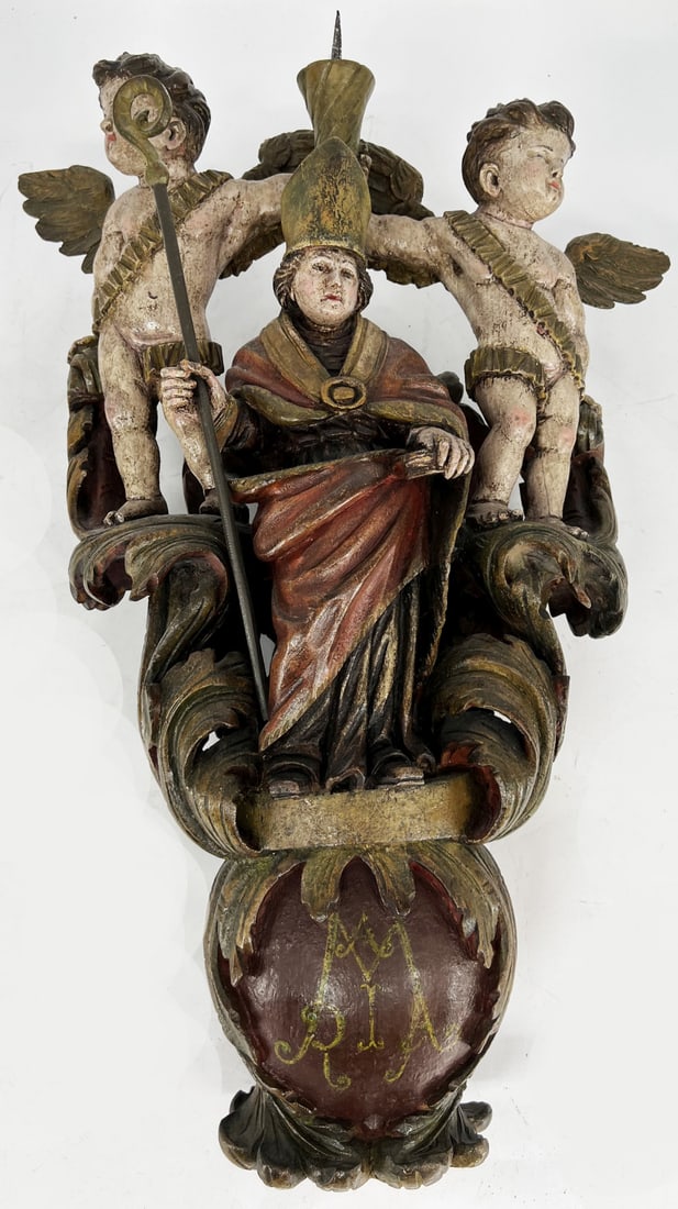 Group of figures on a procession pole: Group of figures on a procession pole: bishop flanked by two angels holding a candlestick, embedded in arcanus leaves, inscription ‘Maria’ on the base, signs of age, height 71 cm (group of