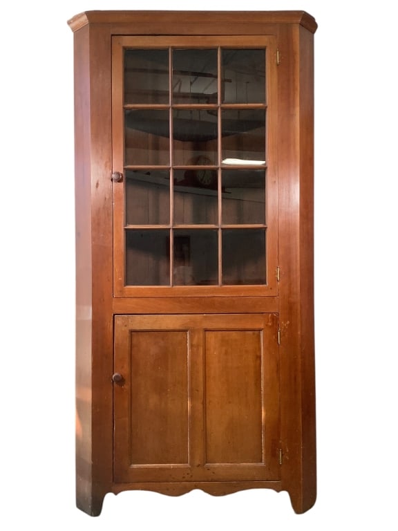 Antique American Cherry Corner Cupboard: 29" x 29" x 84"H, 35 1/4"W face with 12 pane glass panel upper door with fixed shelves, turned knob. Lower cabinet with single recessed panel door. Scroll cut base. Some repairs, cornice has losses