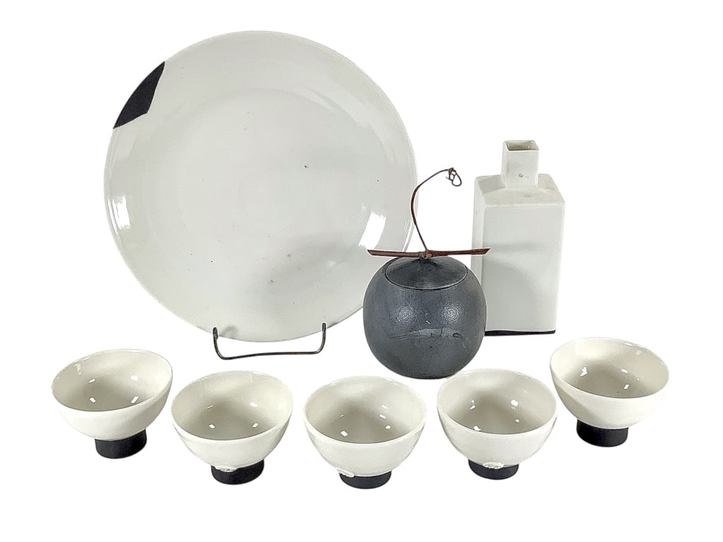 Japanese Porcelain Saki Set w Jar: Signed raku fired jar with twig handle on lid, 3"Dia. 8 1/4" serving plate with 5 - 2 5/8"Dia. cups and 5 3/8"H bottle. 7 matching pieces, all with raised stamp mark. Provenance: Collection of