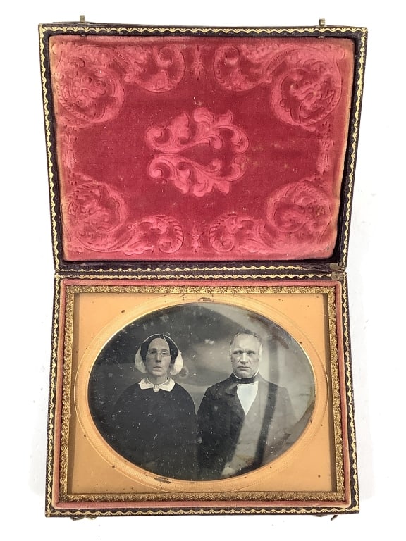 Daguerreotype Portrait of Couple: Daguerreotype portrait of an unknown couple in 3 5/8" x 4 1/2" union case with intact double hooks. Simple oval metal mat and velvet liner. Cover is attached. Tarnish and pitting noted. Wear to