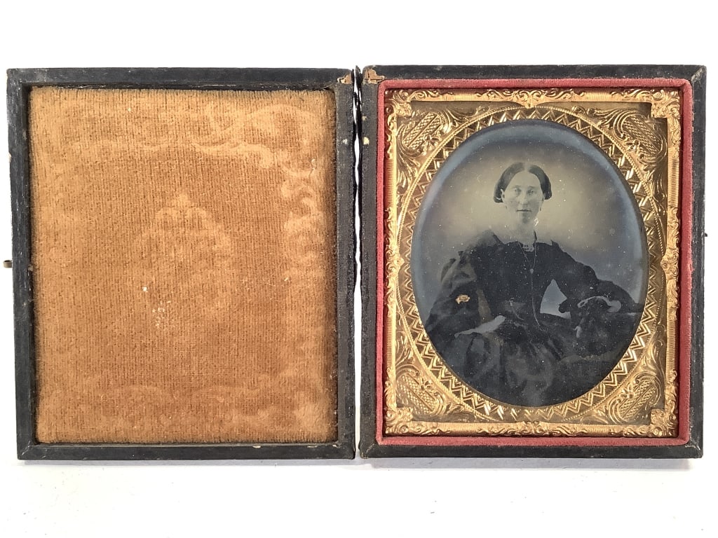Daguerreotype Portrait Formally Dressed Woman: Daguerreotype portrait of an unknown woman in 3 3/4" x 3 1/3" union case with intact hook. Ornate oval metal mat with velvet liner. Tarnish creeping in around edges. Cover is detached but included.