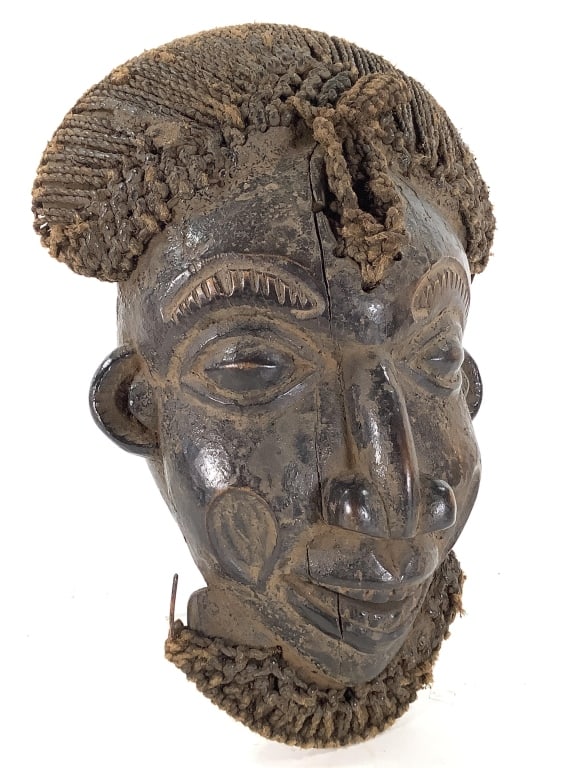 Wood Helmet Mask Bamileke Cameroon Grasslands: 15 1/4" H x 6 1/8"D x 11"W. Bamileke carved wood mask with woven natural fiber hair &a dark rich encrusted patina. Vertical cracks on wood at center and at right eye. Provenance: Collection of