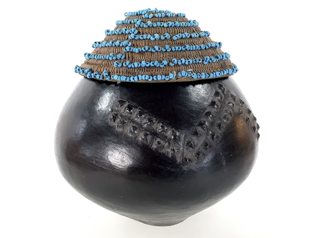 Zulu Earthenware Beer Vessel w Beaded Lid: Small drinking vessel w embossed design, and a smooth black patina. Vessel, 7 3/4"H x 9" Dia. Raffia woven basket lid with beadwork, 7 3/8"Dia. Provenance: Collection of William and Diane Itter.