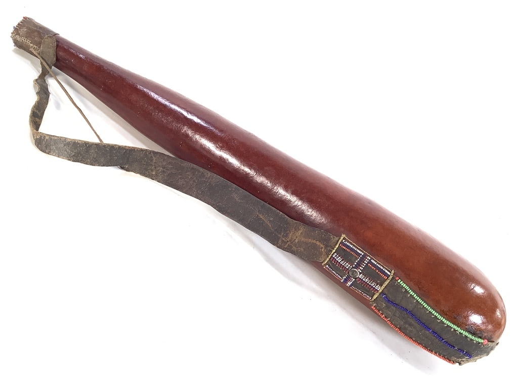 Maasai Beaded Milk Gourd: 25 1/4"L. Polished gourd with leather strap and cap embellished with beadwork. Chip on the lip of the container, some wear on the leather. Provenance: Collection of William and Diane Itter. Please