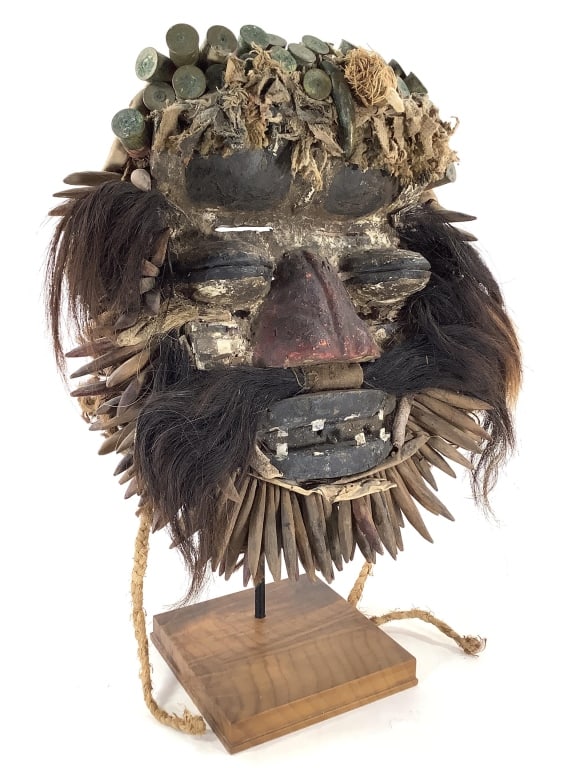 Dan or We / Guere Power Mask West Africa: 16 1/4"H x14 3/4"W x 5 3/4"D (mask), 20 3/4"H on stand. Carved wood mask painted with natural pigments and adorned with plant fibers, animal hair, metal bullet cartridges. Provenance: Collection of Wi