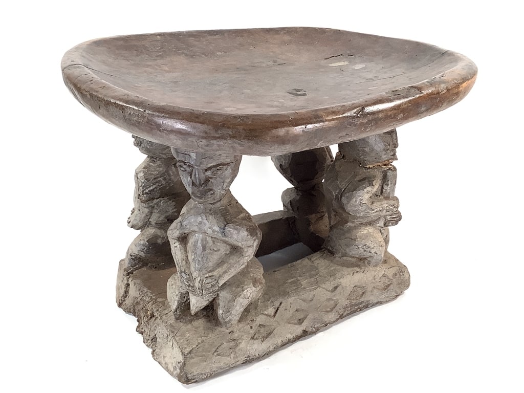 Bamileke Pedestal Stool: 21 1/2"W x 18 1/2"D x 14 3/4"H. Cracks/ fissures on the seat and cracks on the carved figure legs. Provenance: Collection of William and Diane Itter. Please see photos for condition and details.