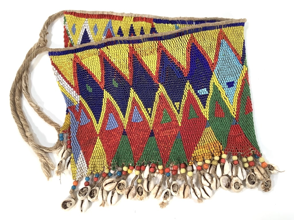 Kirdi Beaded Apron Cameroon: 19 1/2"W x 8 1/2"H excluding the apron string. Kirdi beadwork apron with geometric triangular pattern with cowrie shell and small bead fringe. Some wear on the rope apron string back. Provenance: Coll