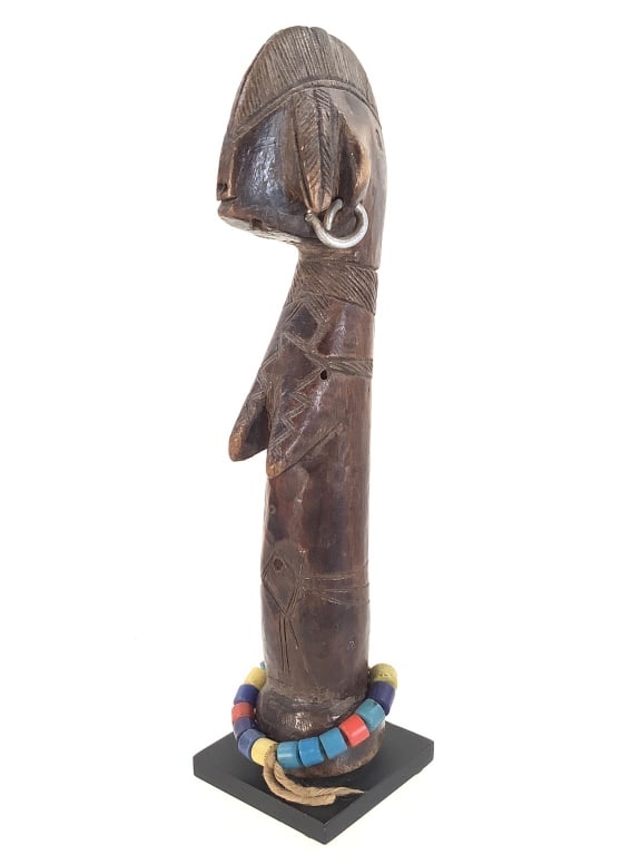 Mossi Doll Burkina Faso West Africa: 1 1/4"W x 8"H. Carved wood with incised surface design. Mounted onto a metal base. Adorned with beads and metal ear rings. Small chip at crown. Provenance: Collection of William and Diane Itter.