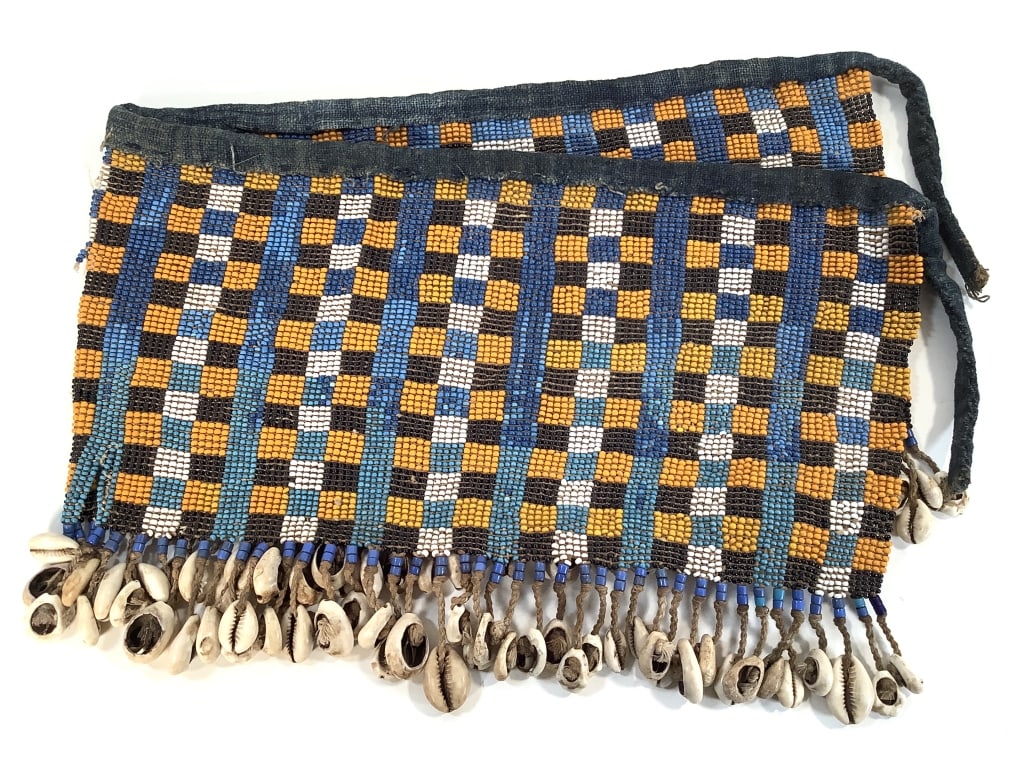 Kirdi Beaded Apron Cameroon: 27"W x 9"H excluding apron tie. Kirdi beadwork apron with an intricate geometric checkered and strip pattern with cowrie shell and small bead fringe and a top edge and tie of fabric. Middle at bottom 