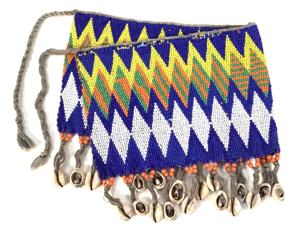 Kirdi Beaded Apron Cameroon: 18 1/2"W x 8 5/8"H excluding apron tie. Kirdi beadwork apron with a diamond and stripes geometric pattern, and cowrie shell fringe at the bottom. Provenance: Collection of William and Diane Itter.