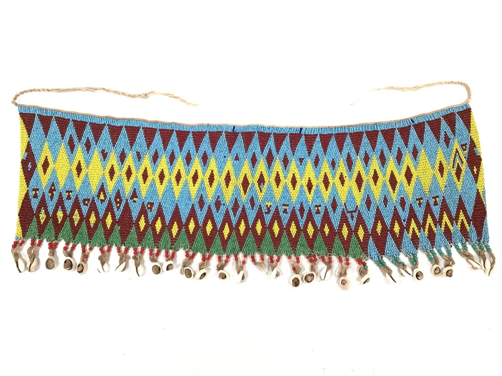 Kirdi Beaded Apron Cameroon: 26" x 9" 23" x 10 3/4" excluding apron tie. Kirdi beadwork apron with an diamond weave geometric pattern, and cowrie shell fringe at the bottom. One cowrie shell missing on bottom center fringe.