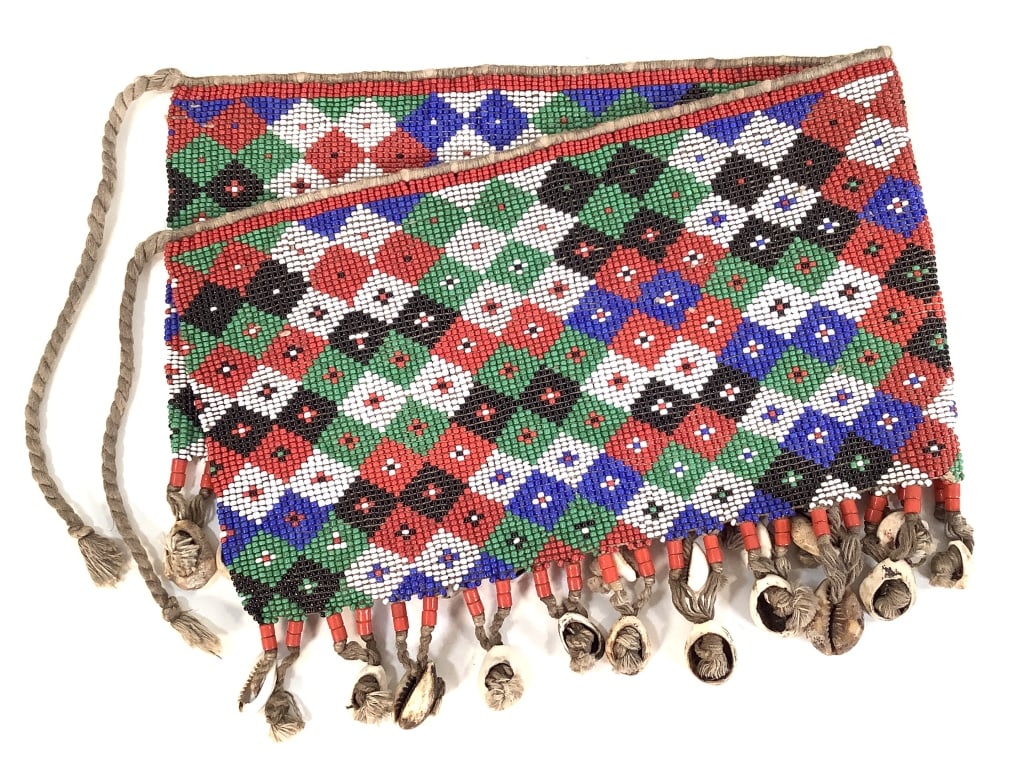 Kirdi Beaded Apron Cameroon: 20 1/4" x 7 3/4". 23" x 10 3/4" excluding apron tie. Kirdi beadwork apron with an intricate diamond lattice pattern, and cowrie shell fringe at the bottom. Provenance: Collection of William and Diane 
