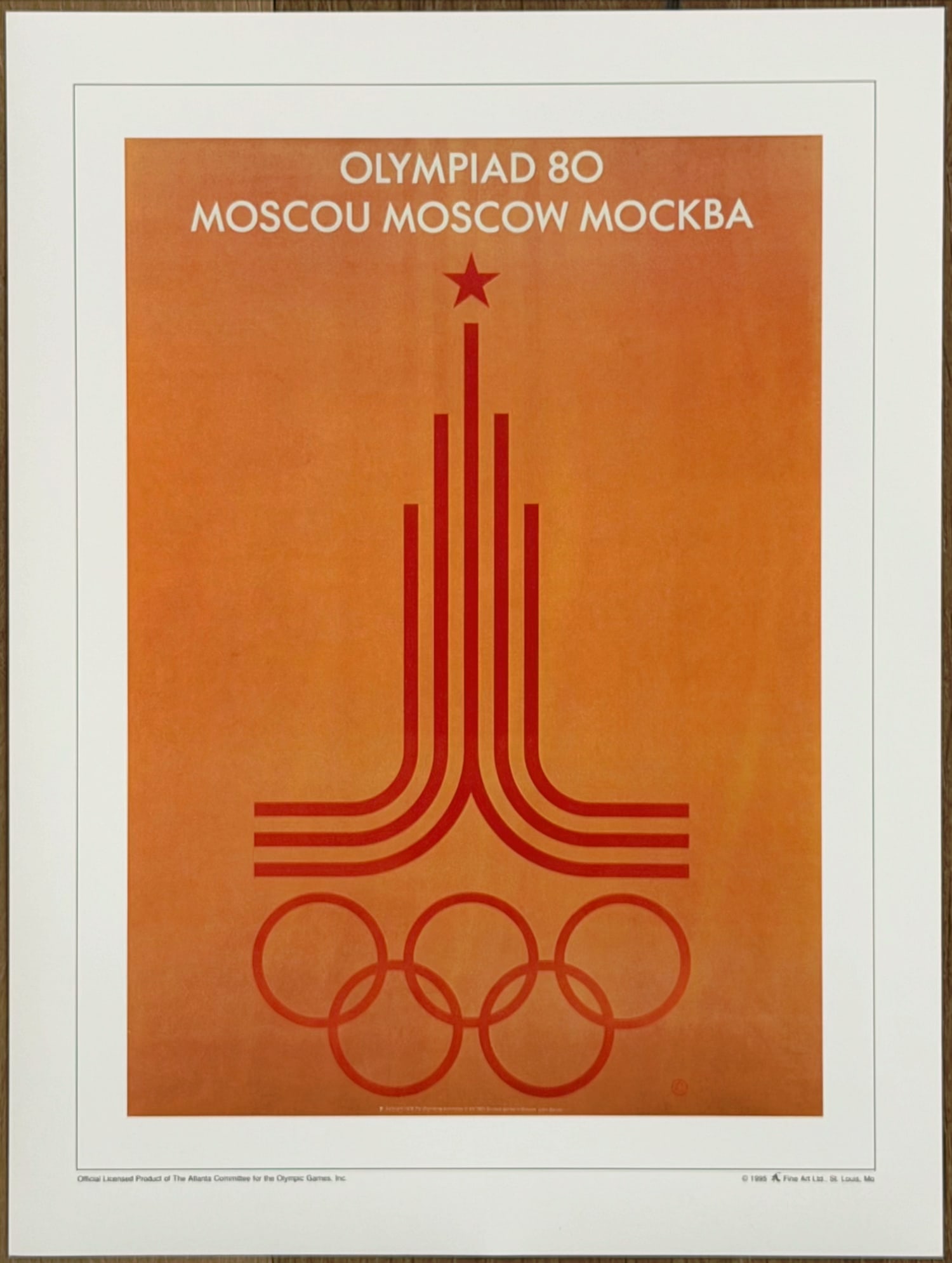 1980 Moscow Olympic Games Official Poster – Emblem Design Print: Official licensed print of the 1980 Moscow Olympic Games poster. Features the iconic emblem of stylized running tracks rising into a tower topped with a red star, above the Olympic rings, on a warm be