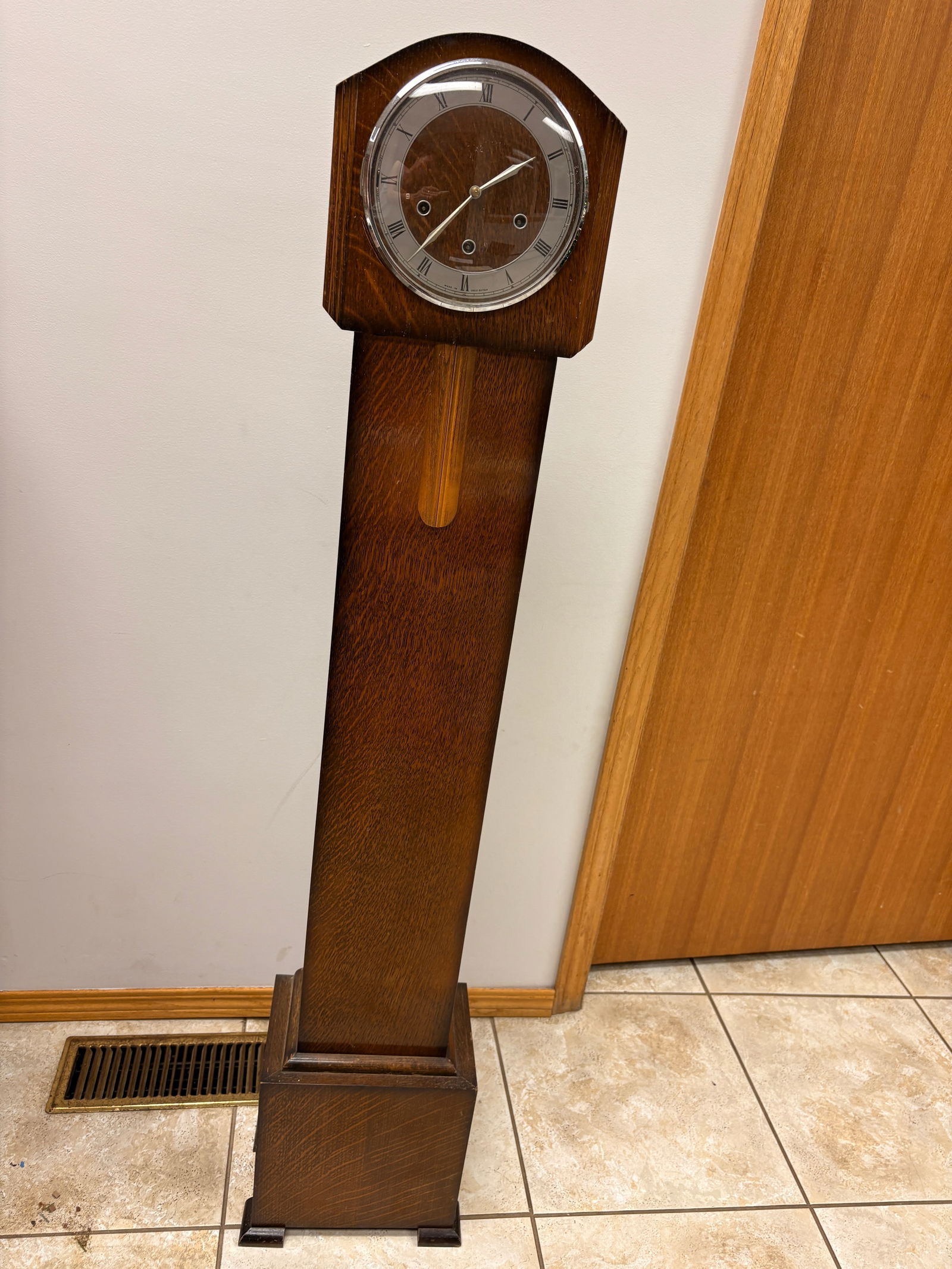 British Granddaughter Clock: Elegant British tall case clock with a clean, minimalist mid-20th-century design. Solid wood case with warm original finish, silvered chapter ring with Roman numerals, and three winding arbors