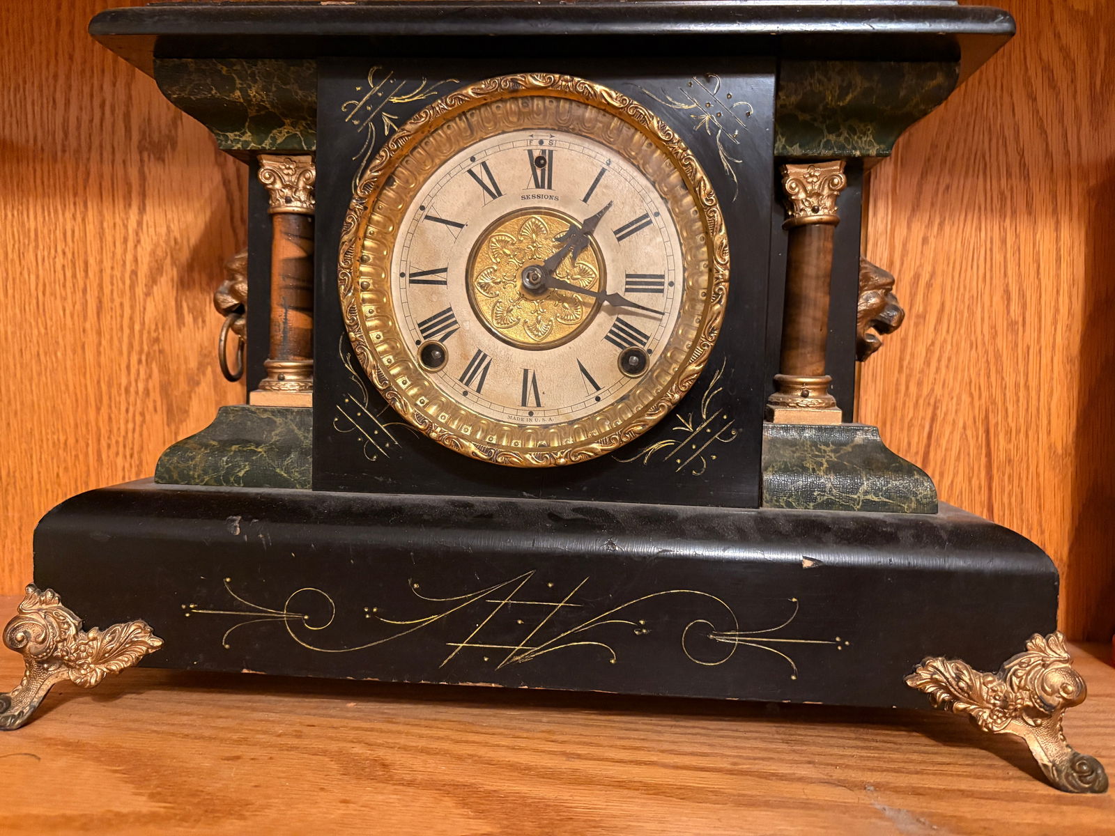 Ornate American Mantel Clock with Lion Masks: Highly decorative American mantel clock, early 20th century. Black case with rich gilt floral decoration, marble-style accents, and striking lion head masks on both sides. Original Roman numeral dial