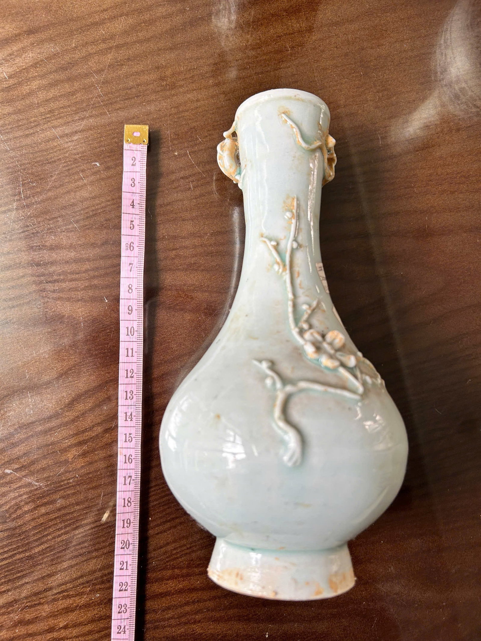 Chinese Celadon-Glazed Relief Vase, Yuan–Ming (14th–15th Century): Baluster-form vase with tall flaring neck, covered in a pale celadon glaze. The body is decorated in molded relief with flowering branches and scrolling vines, complemented by applied handles at the n