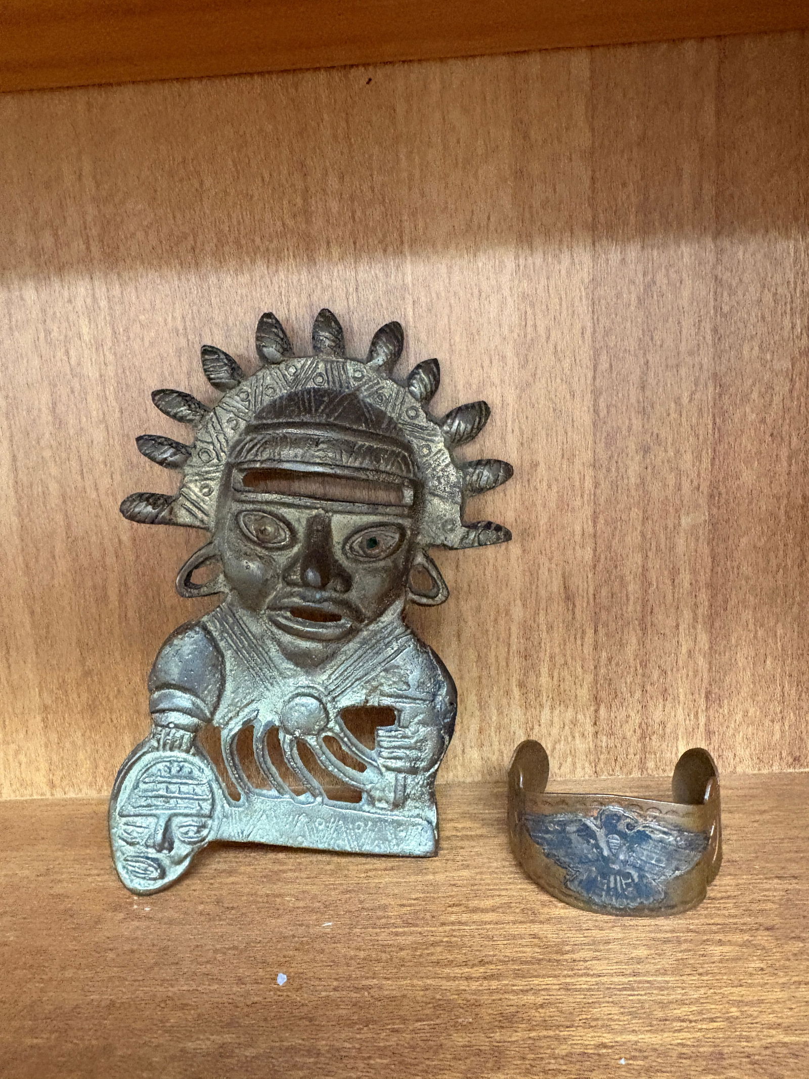 Indigenous-Cast Metal Mask & Engraved Cuff Bracelet: Cast metal mask with stylized headdress and pierced details, accompanied by an engraved metal cuff bracelet featuring symbolic motifs. Natural patina and age wear consistent with use and display.