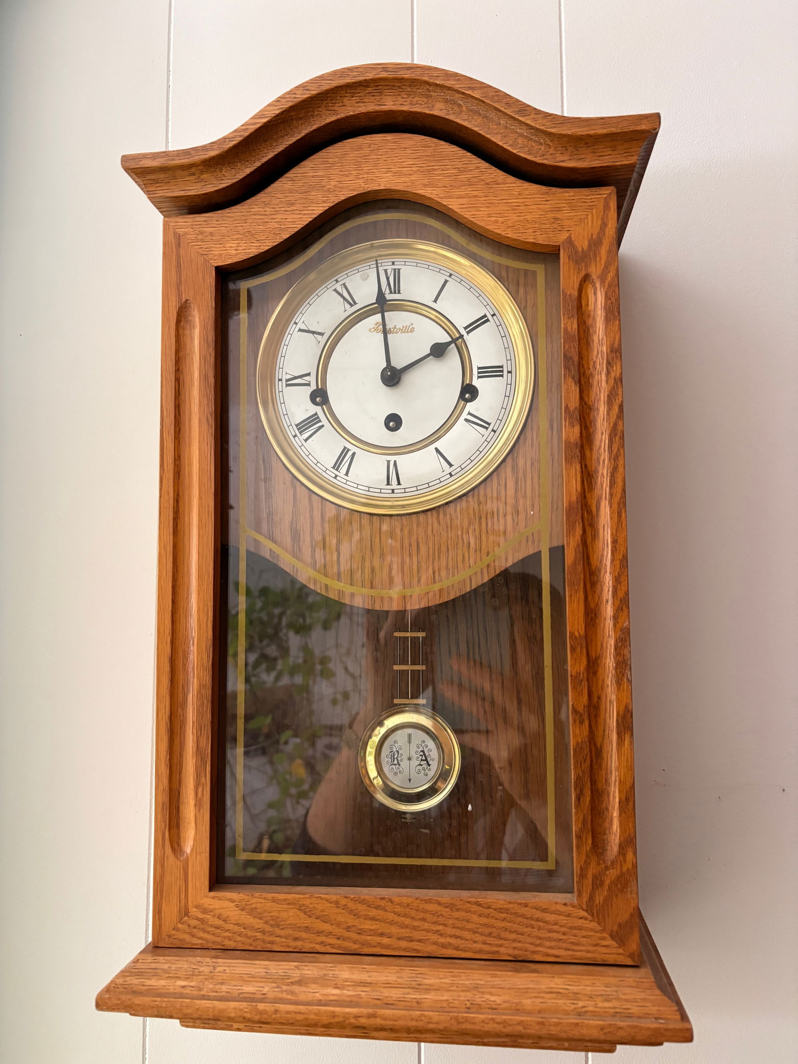 Forestville Oak Wall Clock with Pendulum: Vintage wooden wall clock in solid oak case with glass door and brass accents. White dial with Roman numerals, mechanical movement with pendulum. Clean classic design, wall-mounted. Runs and keeps