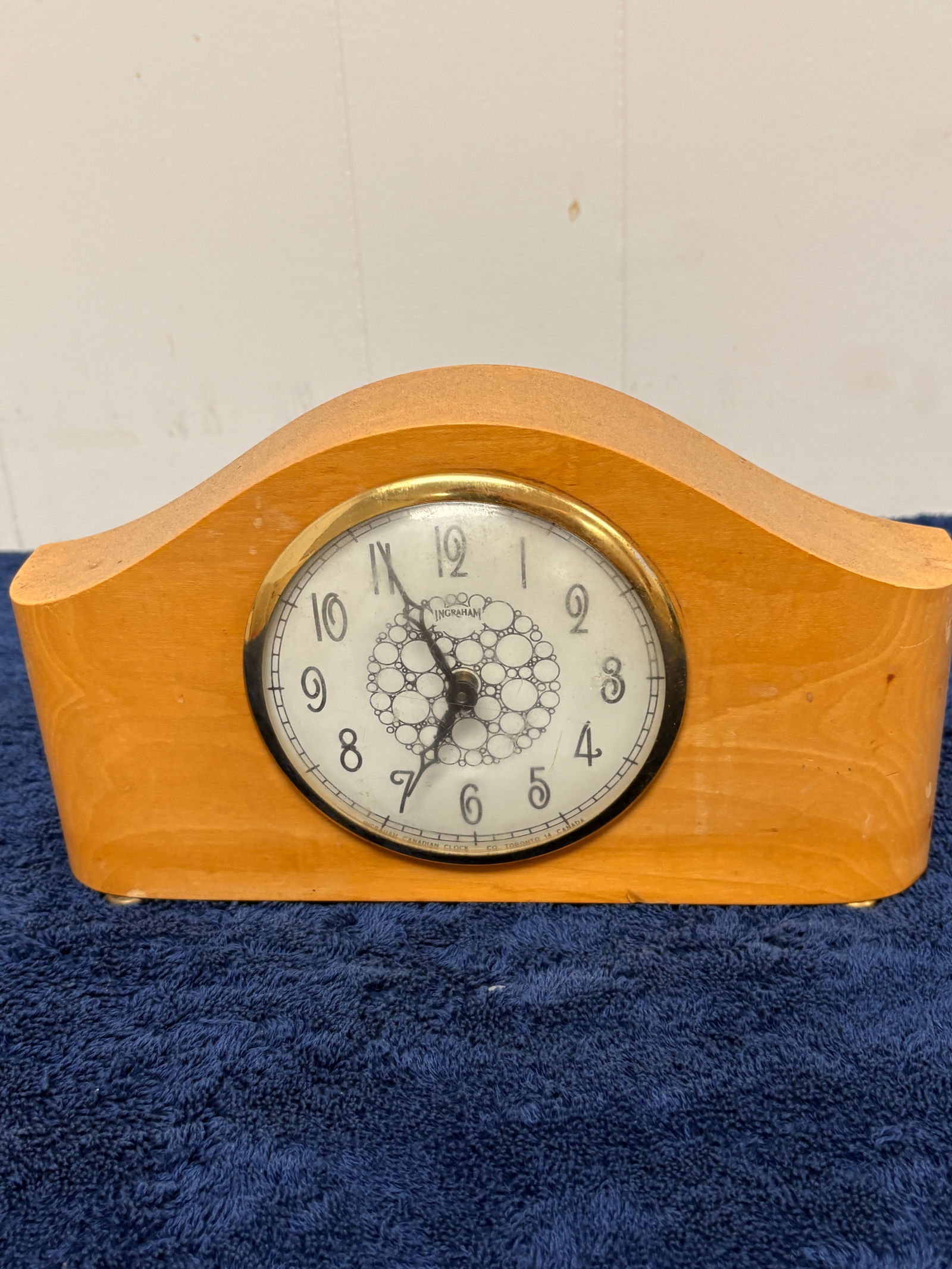 Vintage Ingraham Mantel Clock, Canadian Made: Charming vintage mantel clock by Ingraham, featuring a warm wooden case with elegant curved profile and original brass bezel. Cream dial with bold Arabic numerals and distinctive decorative center