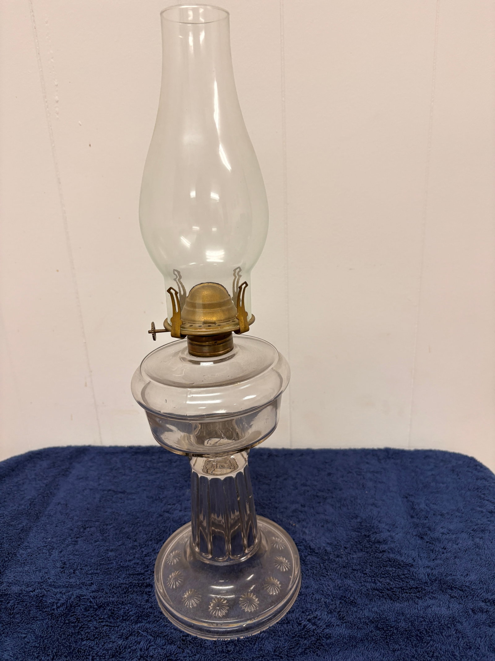 Antique Pressed Glass Kerosene Table Lamp, c. 1900–1920: Antique clear pressed-glass kerosene table lamp featuring a faceted reservoir, fluted column stem, and starburst-pattern circular base. Fitted with a brass burner and a tall clear glass chimney. Class