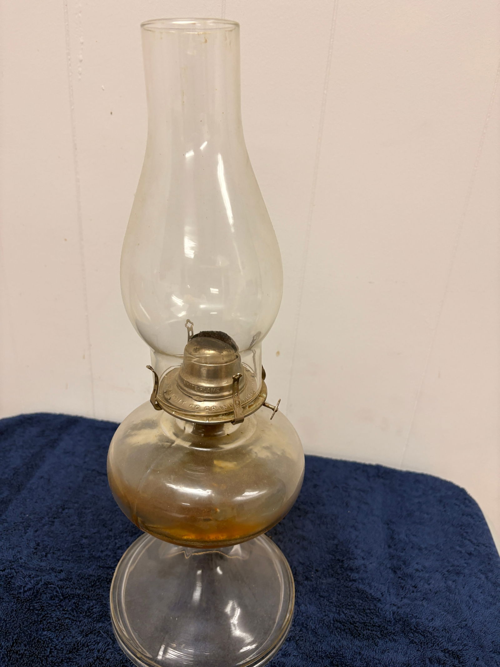 Early 20th Century Pressed Glass Kerosene Table Lamp: Antique kerosene table lamp featuring a clear pressed-glass font with warm amber fuel patina, paired with a faceted stem and octagonal stepped base. The lamp is fitted with an early brass burner marke