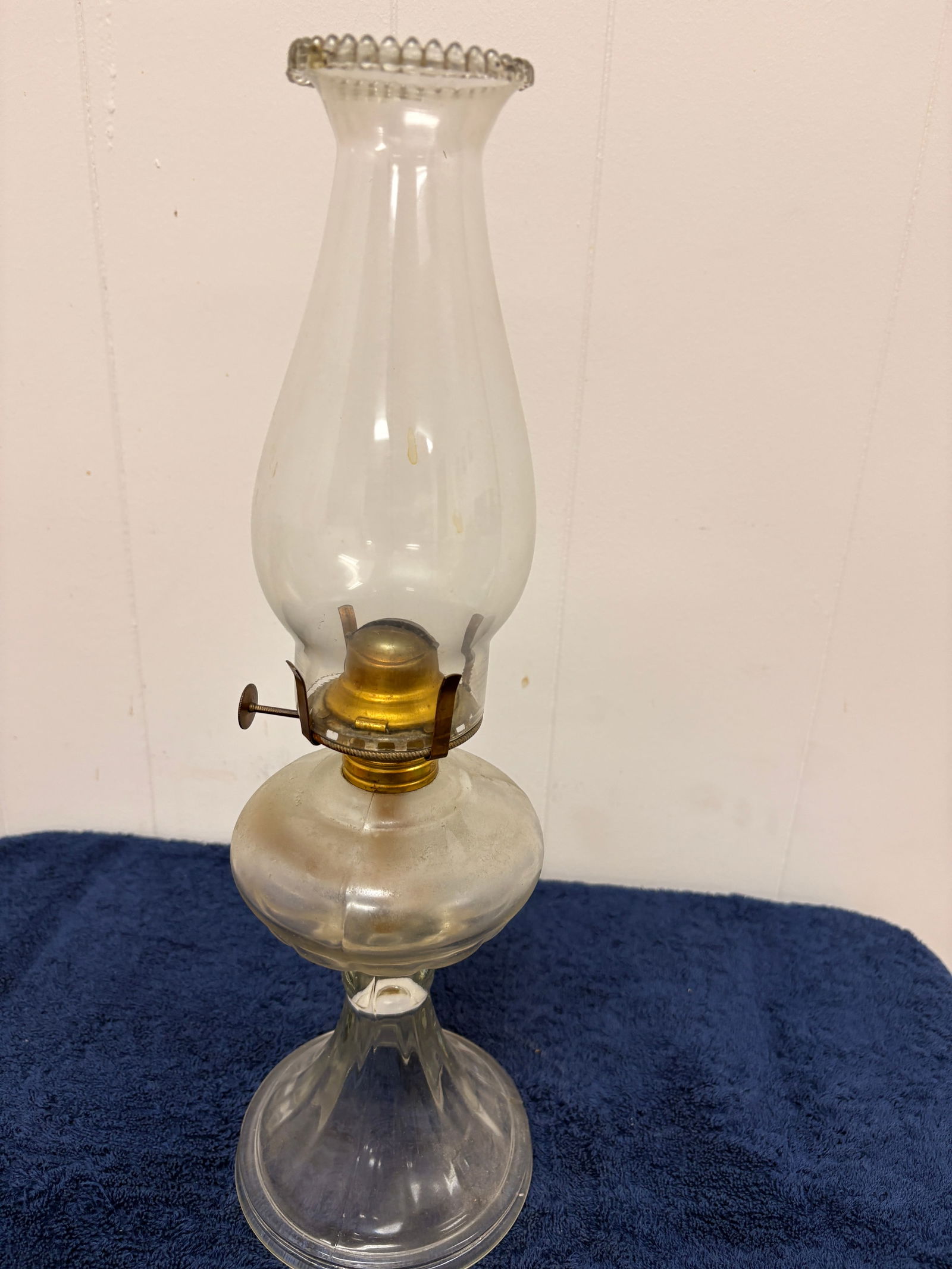 Early 20th Century Clear Glass Kerosene Lamp with Beaded Chimney: An early 20th-century kerosene lamp featuring a clear blown-glass font on a shaped pedestal base. Fitted with a brass burner and a tall clear chimney with a beaded rim, adding a subtle decorative acce