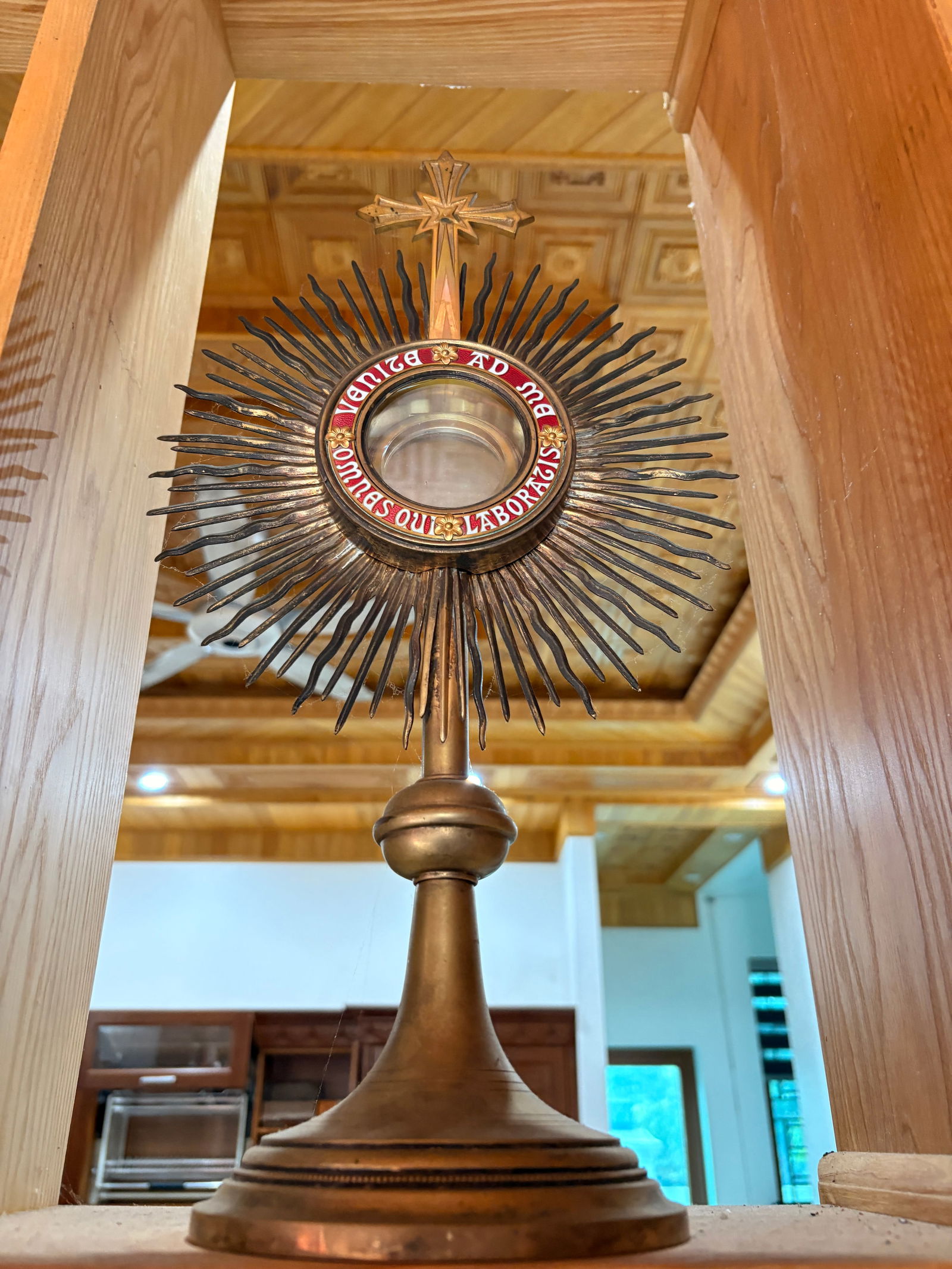 Antique French Monstrance, 19th Century: A striking antique French monstrance dating to the 19th century, featuring a classic radiant sunburst design with a central glazed luna surrounded by red and blue enamel lettering reading “Venite